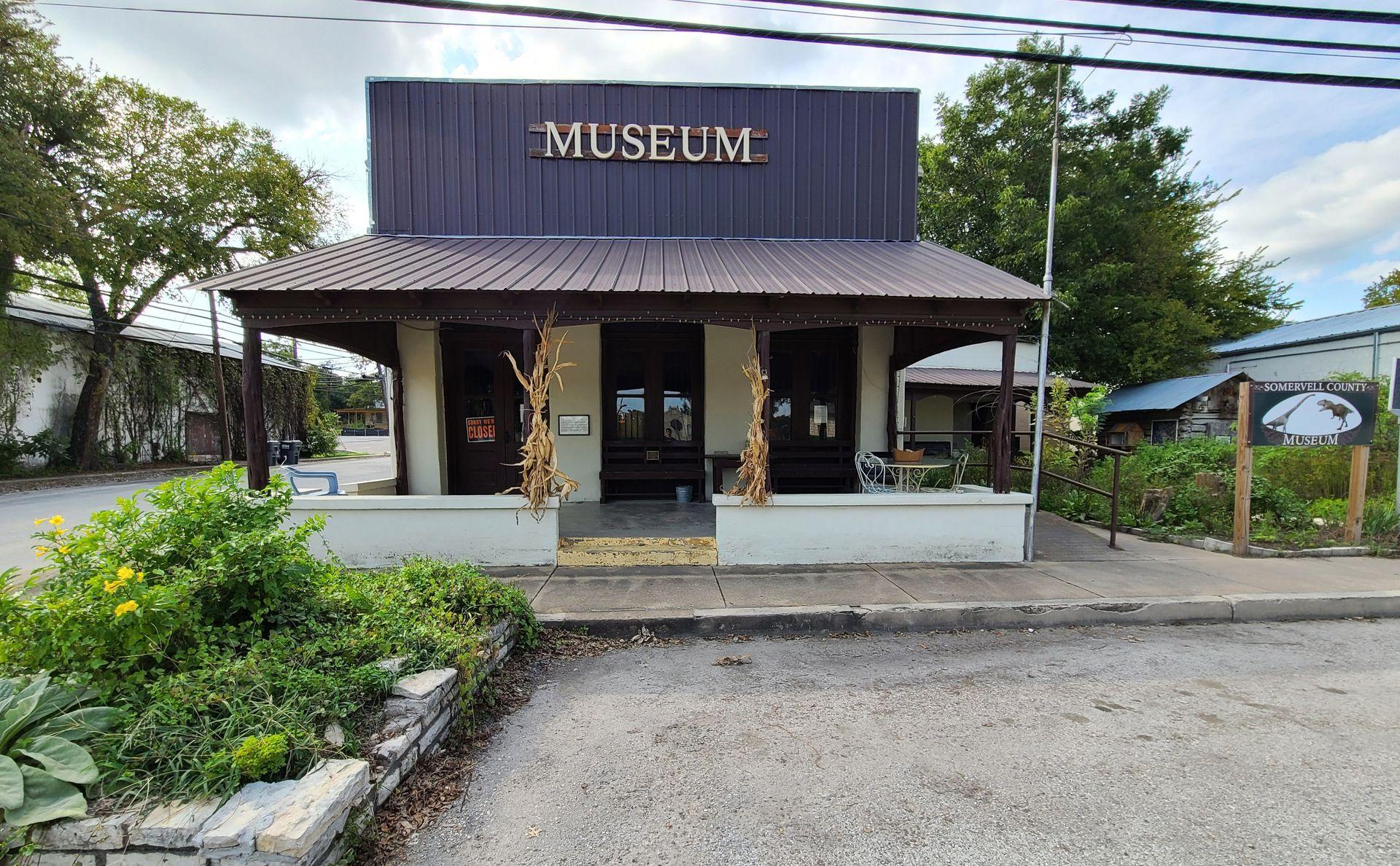 A small building labeled 'museum' with some green plants in the front and the on right side.