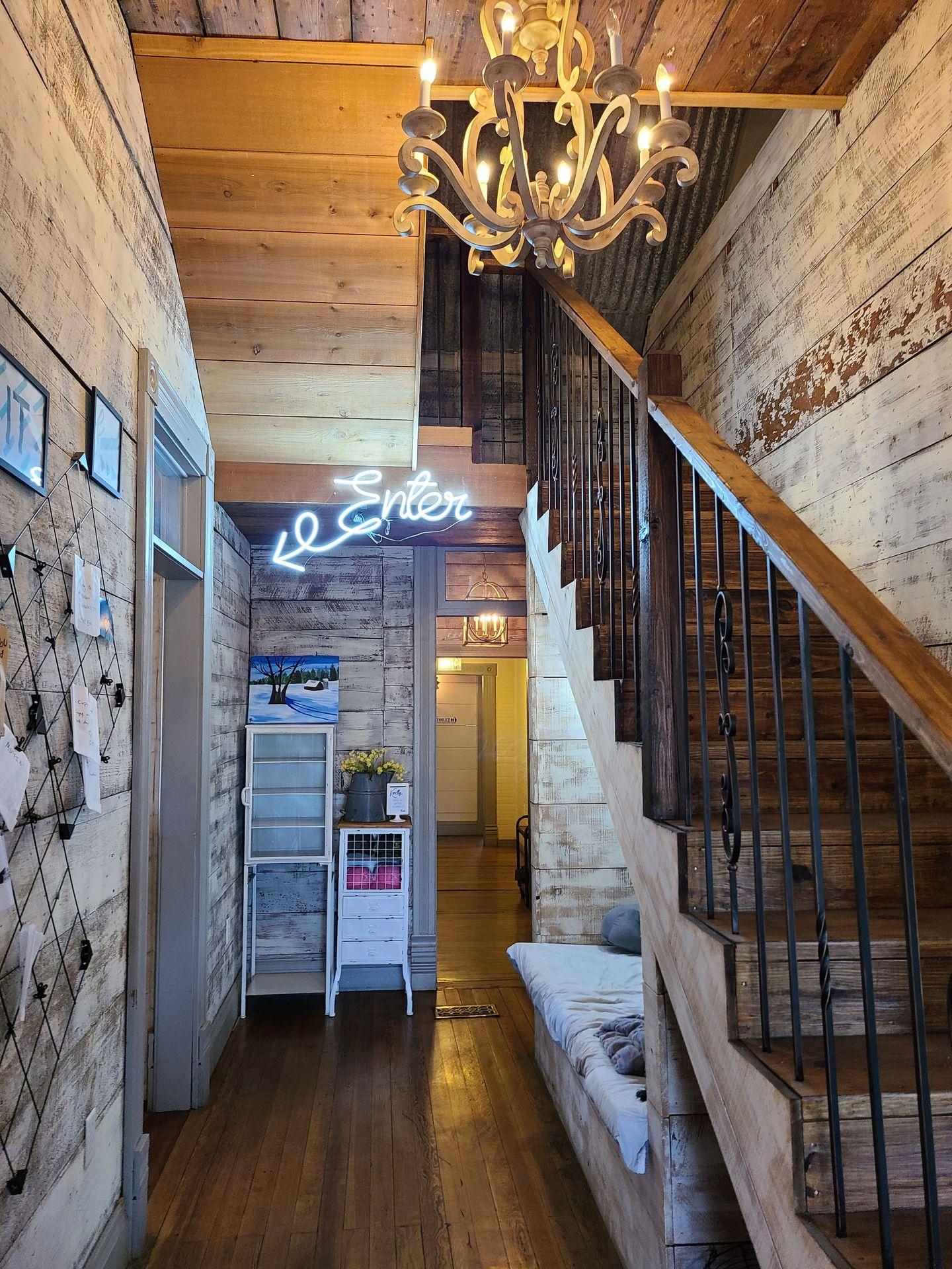 The interior of 2nd Street Bakeshop. There is a staircase, a chandelier and distressed wood on the walls. In the back of the hallway, a neon sign reads Enter with an arrow pointing left.