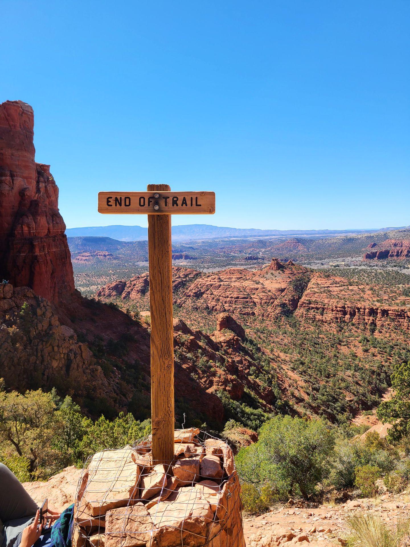 A sign that reads "End of trail" with the views from Cathedral Rock in the distance.