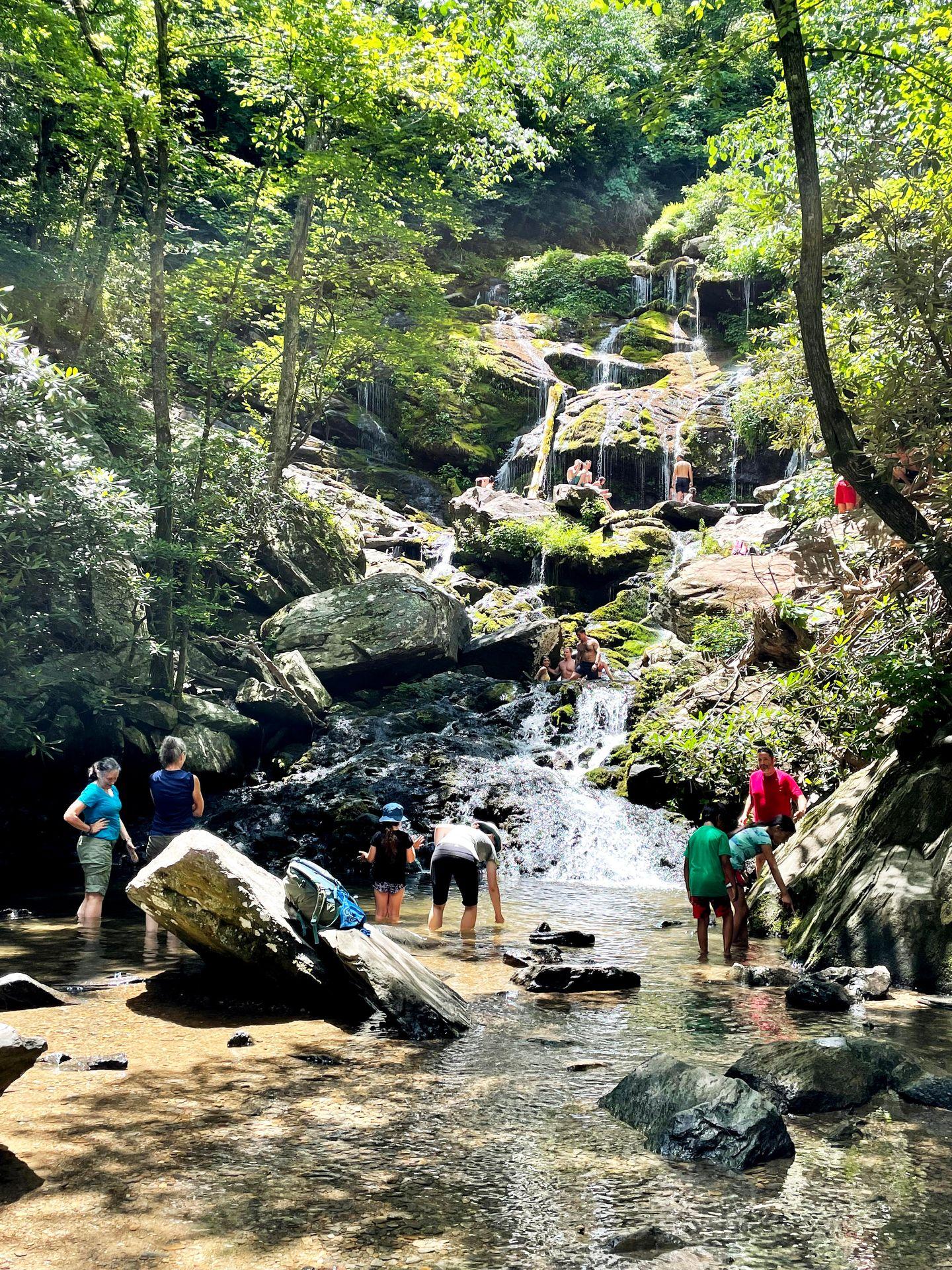 Several people standing in front of and climbing on Catawba Falls.