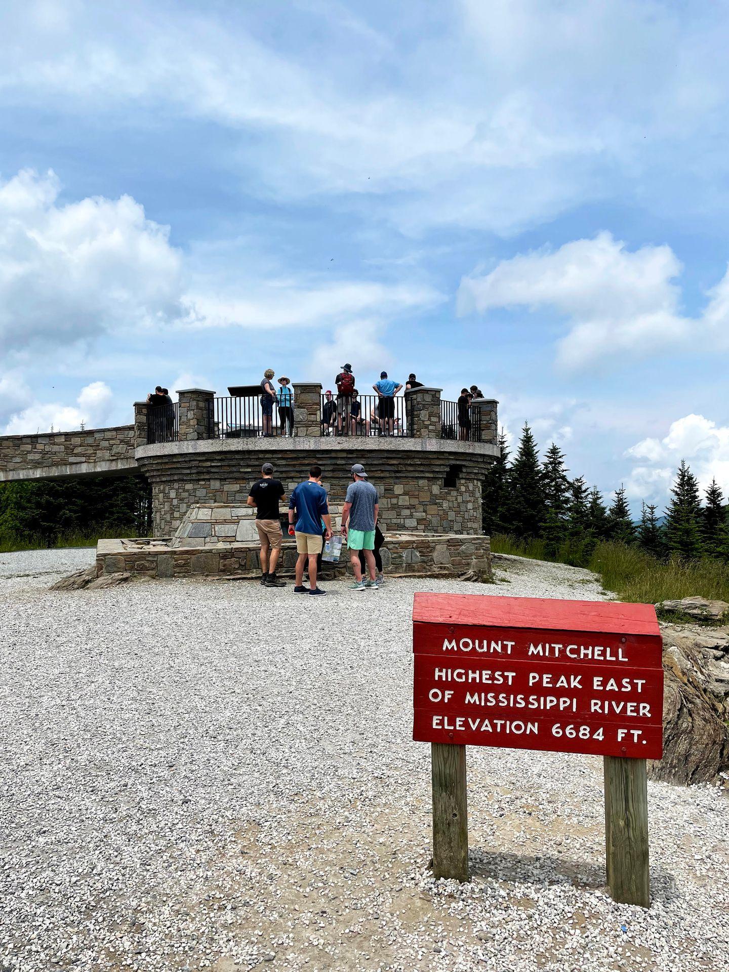 A sign for the top of Mount Mitchell and a viewing platform in the background.