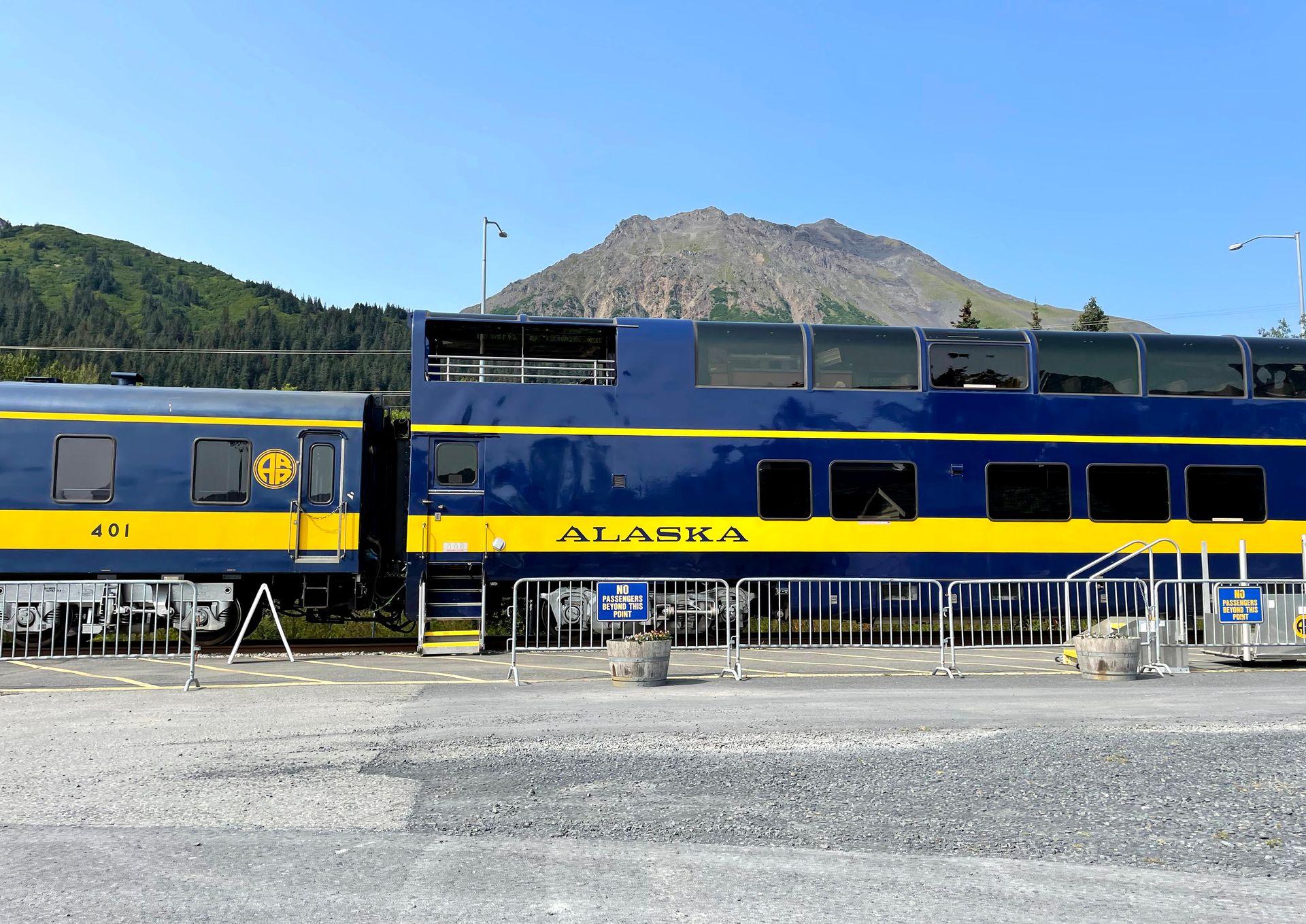 A blue and yellow train part of the Alaska Railroad parked at a station.