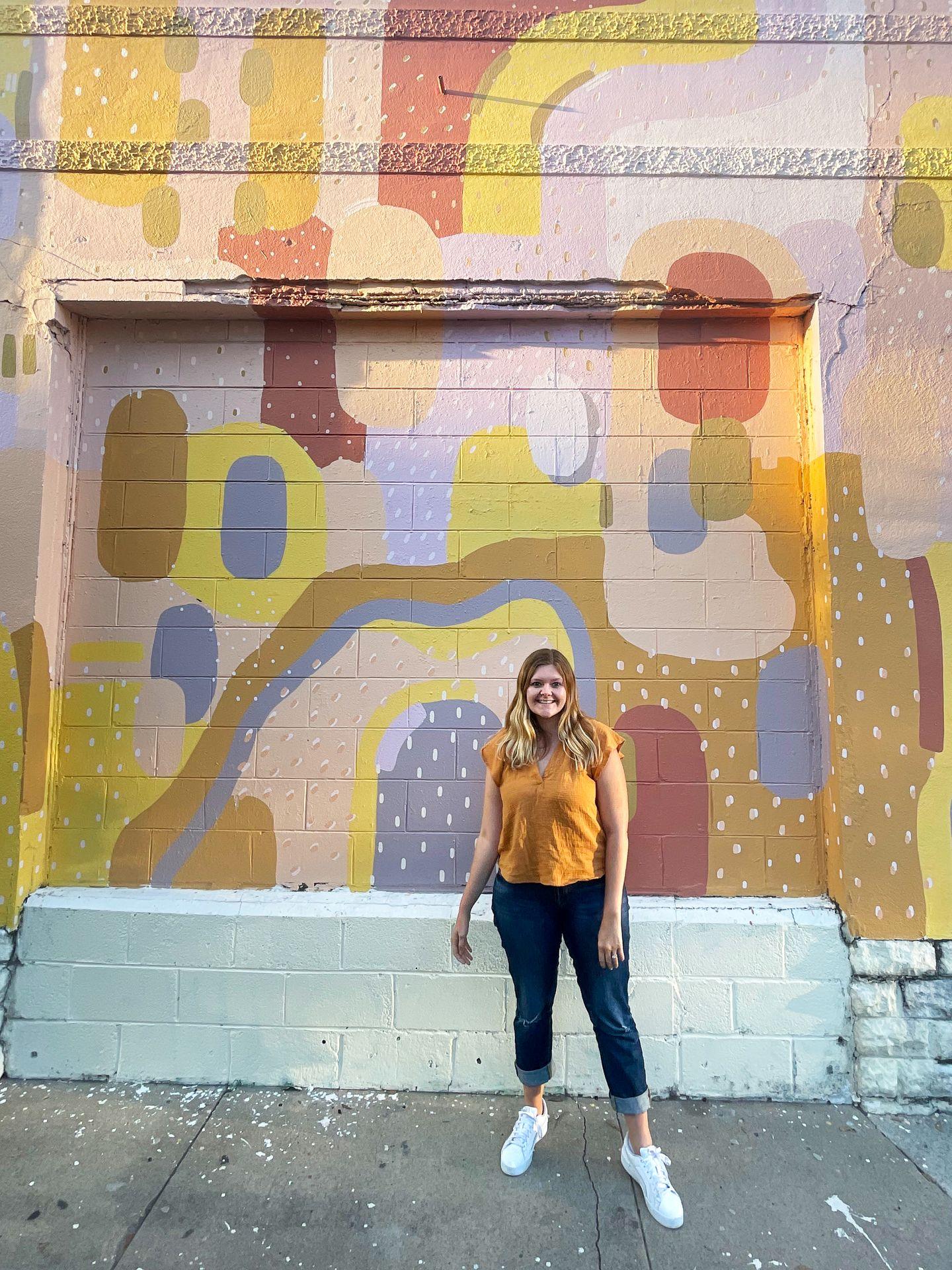 Lydia standing in front of a colorful mural in the Starland District