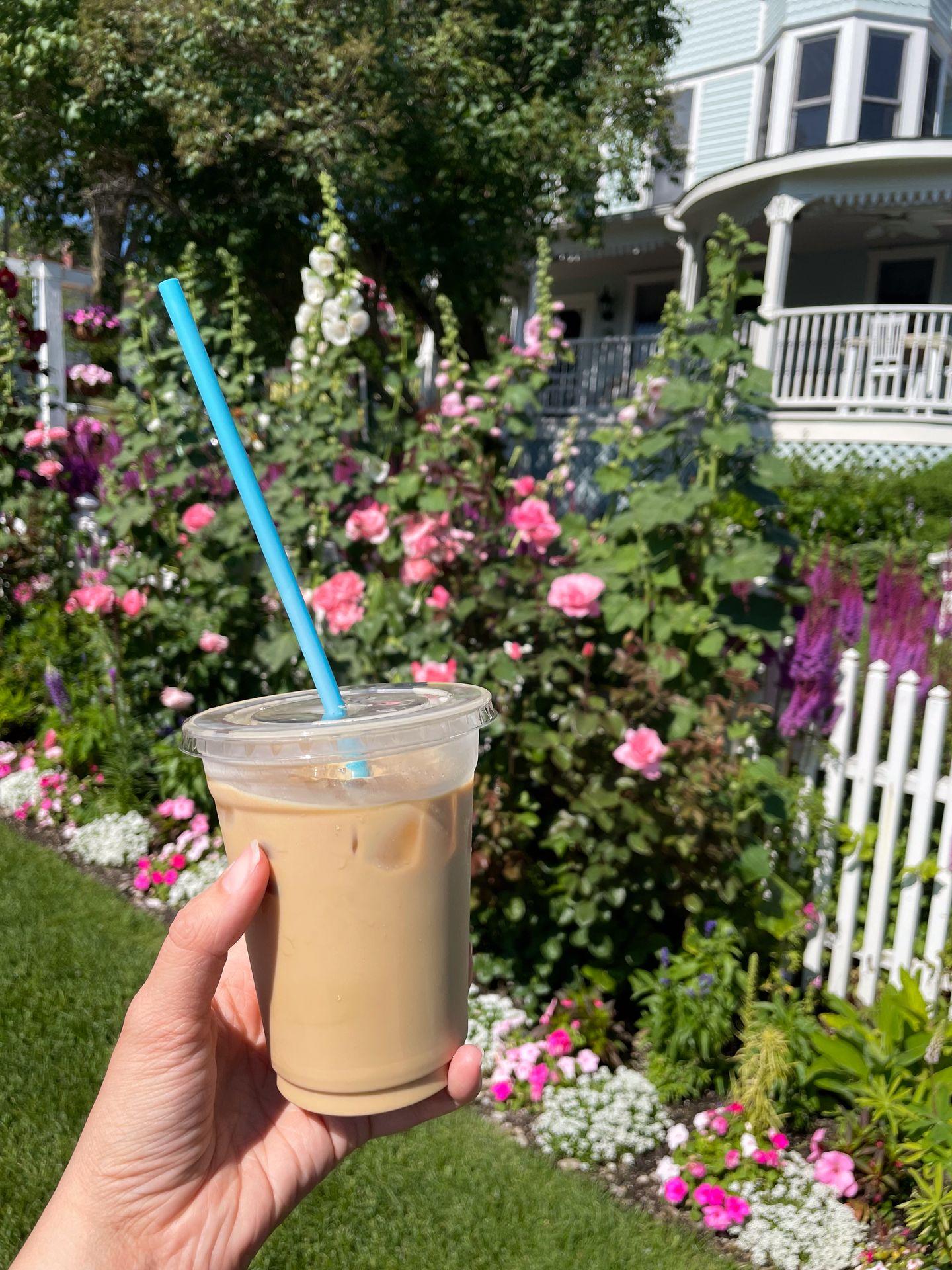 Holding up an iced coffee in front of flowers on Mackinac Island.