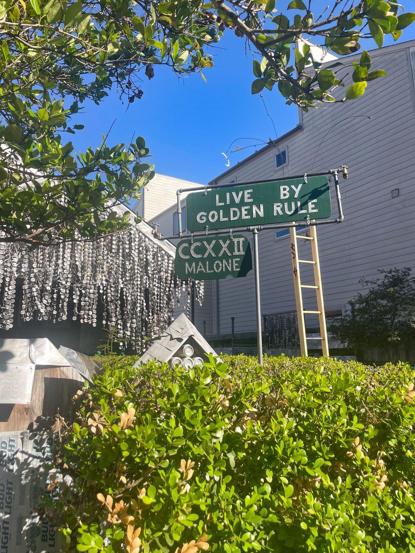 A sign that reads 'Live by golden rule' in front of the Beer Can House