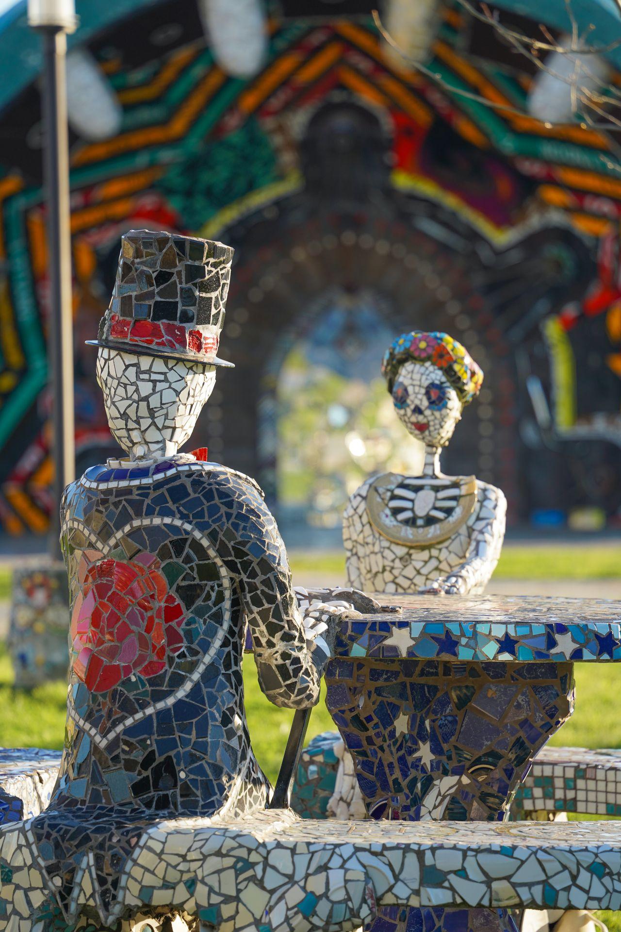 Two skeletons sitting at a table in Smither Park. The skeletons and table are covered in mosaic tiles