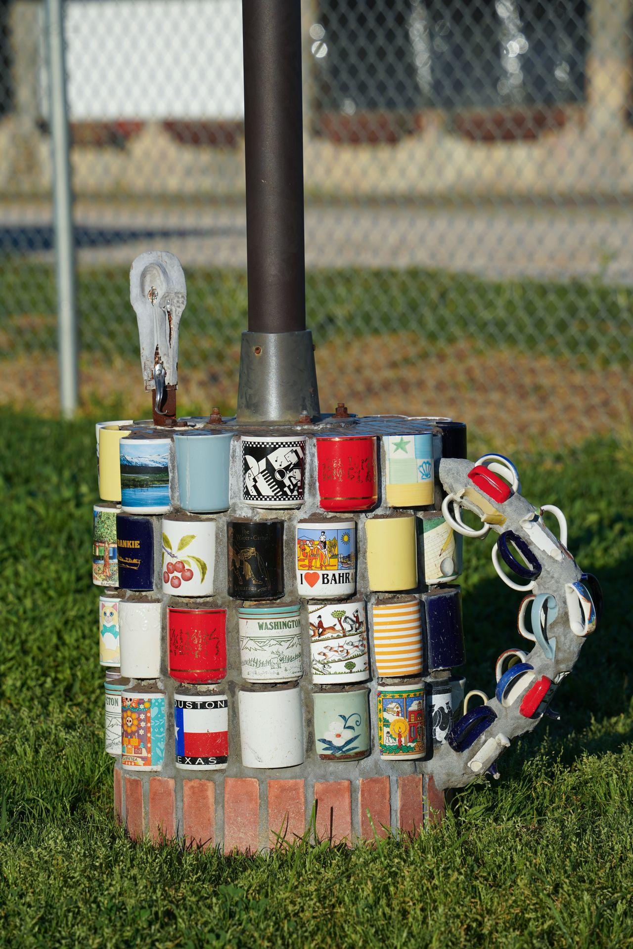 The base of a lamppost, which is shaped like a giant mug made up of many smaller mugs