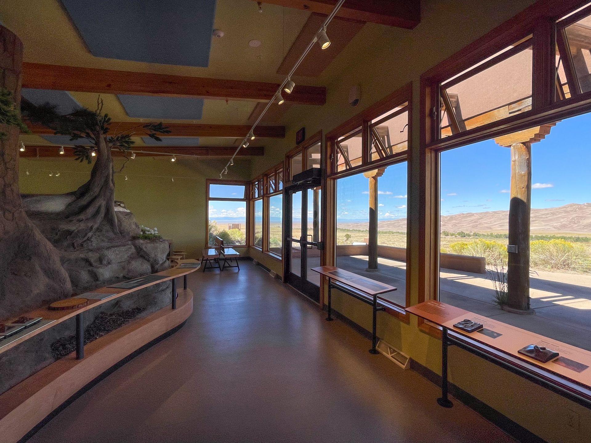 An interior space with signage and displays educating visitors on Great Sand Dunes. You can also see the sand dunes through the window.