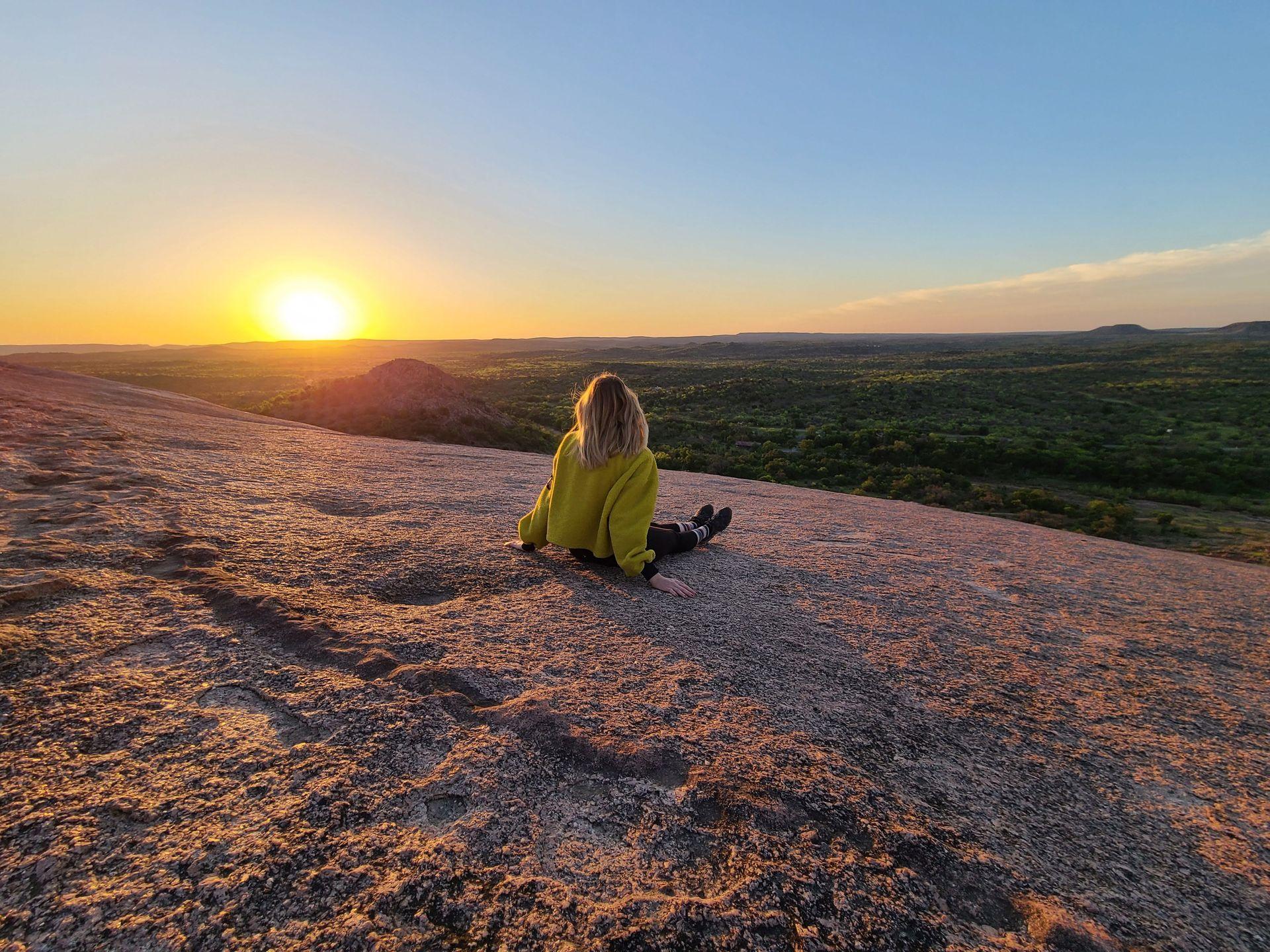 Lydia sitting on Enchanted Rock with her back to the camera watching the sunrise.