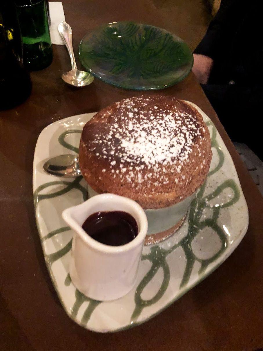 A desert souffle topped with powdered sugar. There is a small jar of chocolate sauce next to it.