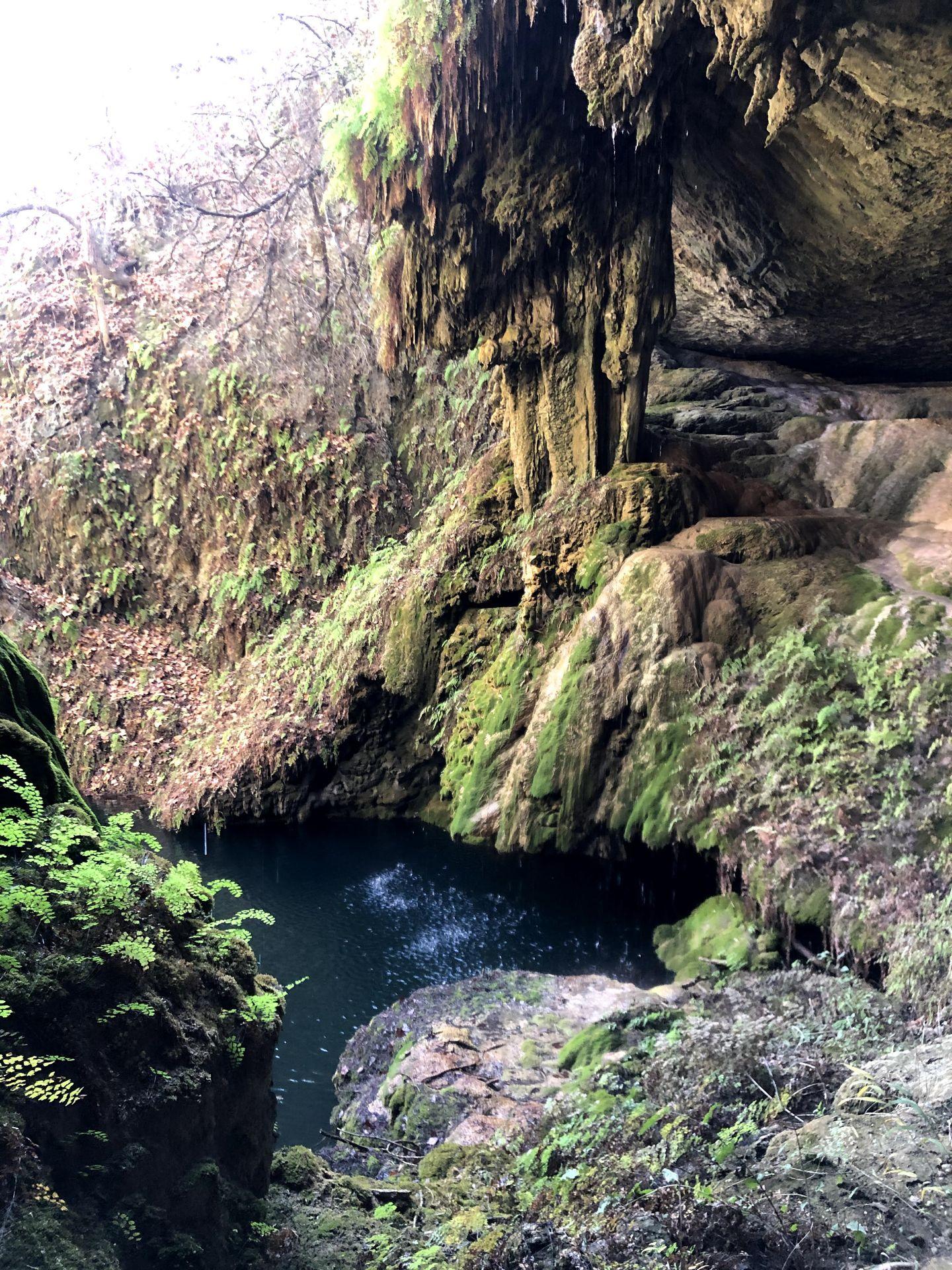 The West Cave grotto, which includes a small pool of water surrounded by green moss.