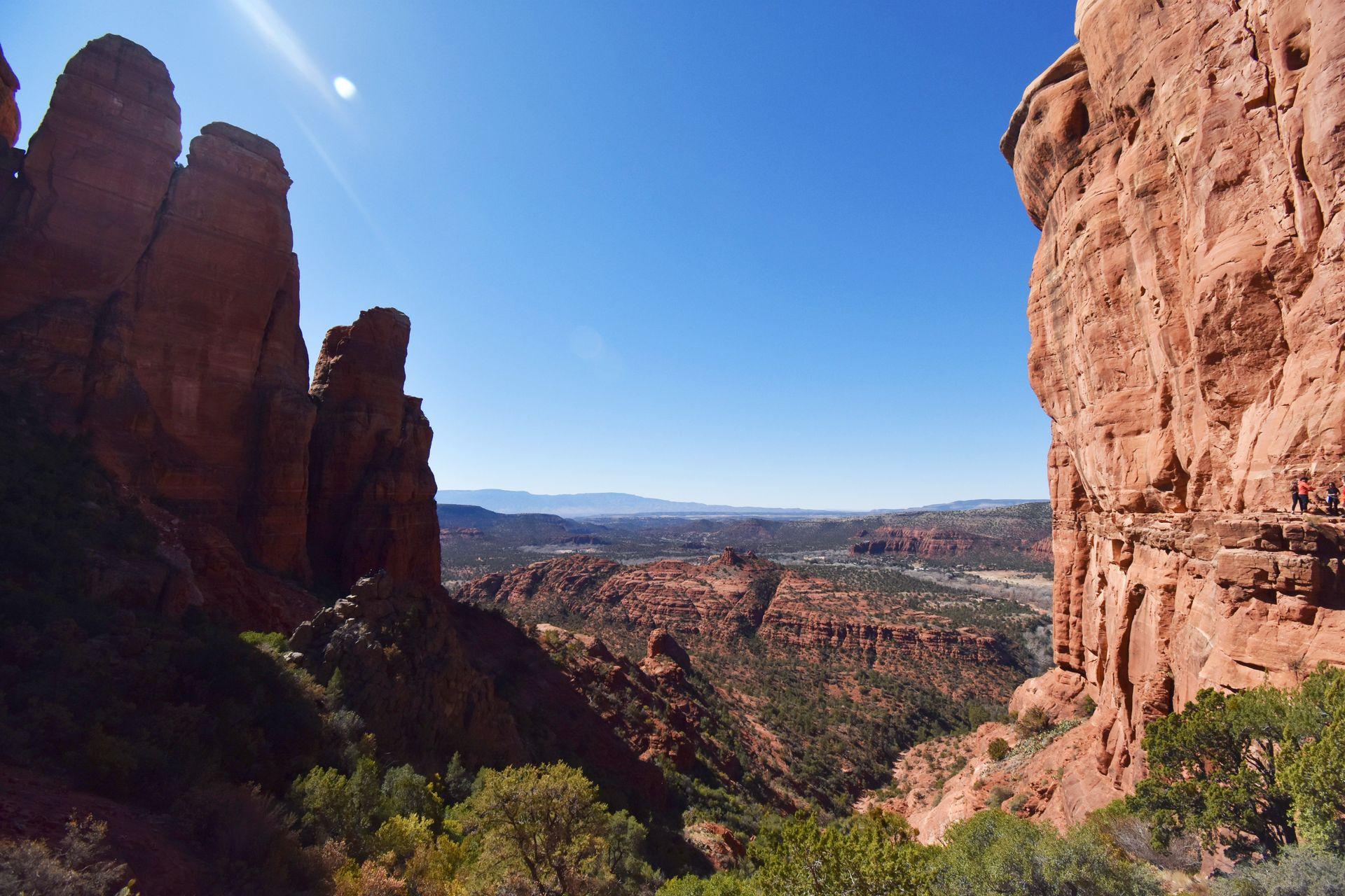 A view of two rock faces on either side with a view of a valley full of red rocks in the center.
