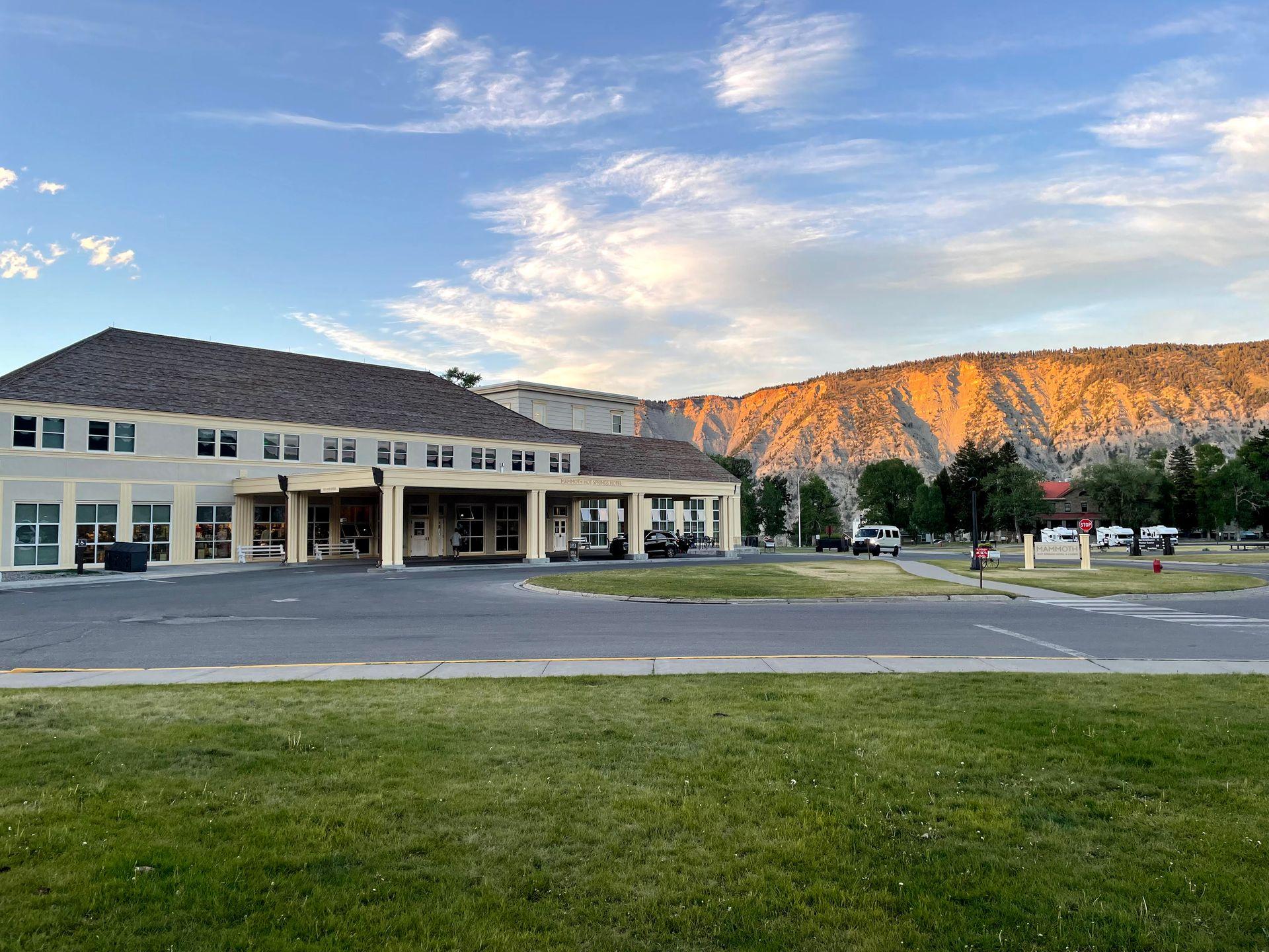 The exterior of the Mammoth Hot Springs Hotel with mountains glowing orange in the background.