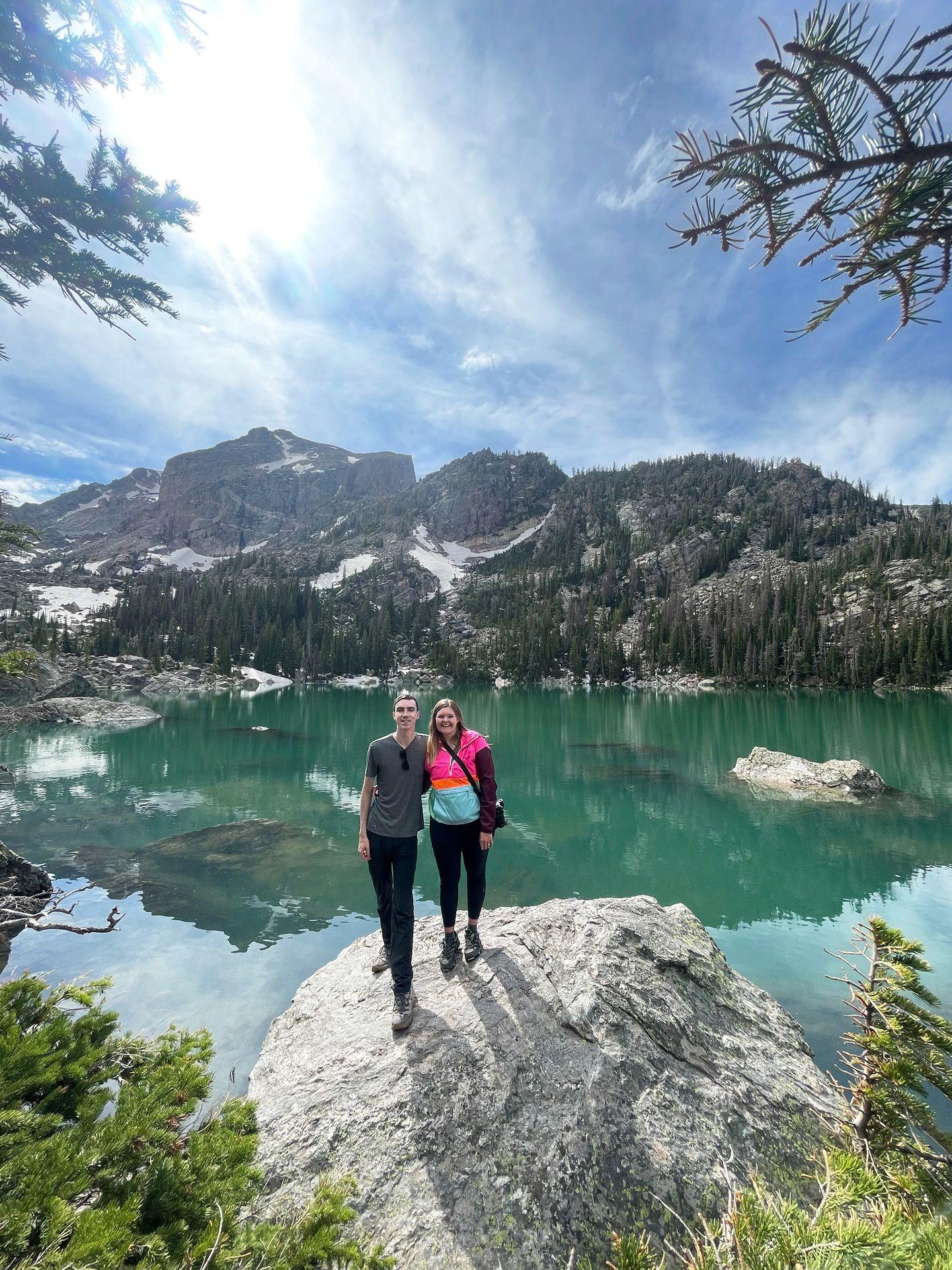 Lydia and Joe standing in front of the aqua, blue water of Lake Haiyaha in Rocky Mountain National Park.