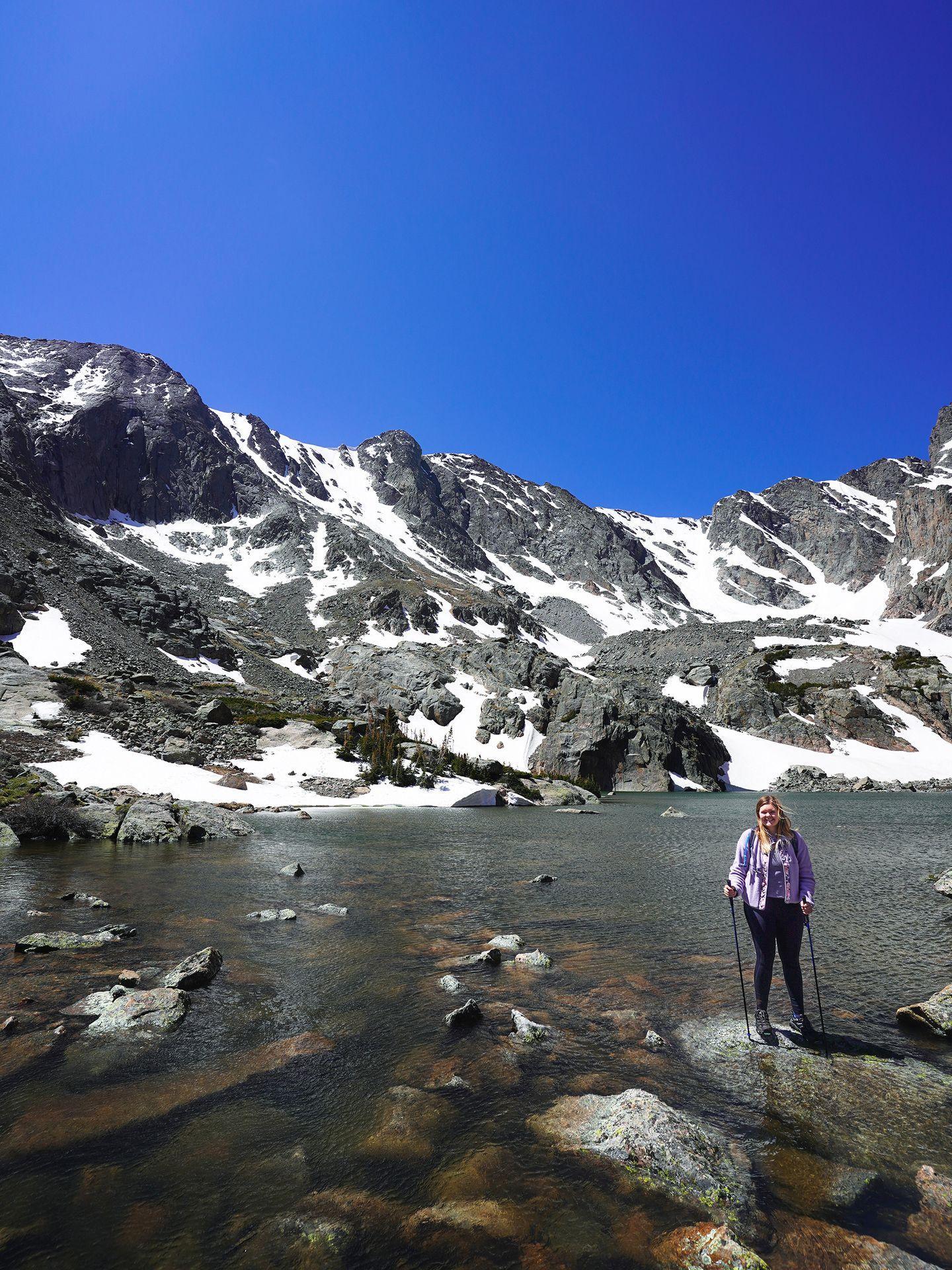 Lydia standing in front of Sky Pond. The mountain in the background is partially covered in snow.