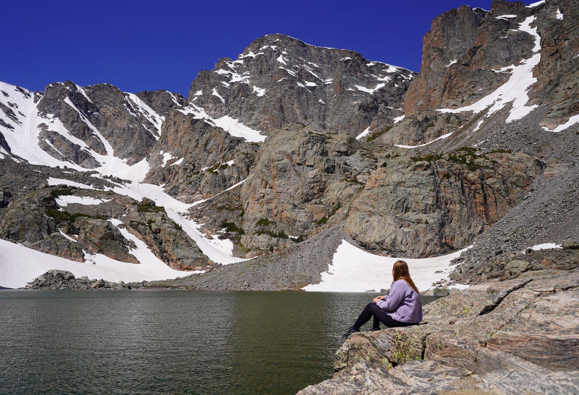Lydia sitting next to Sky Pond. There are various drifts of snow along the mountainside.