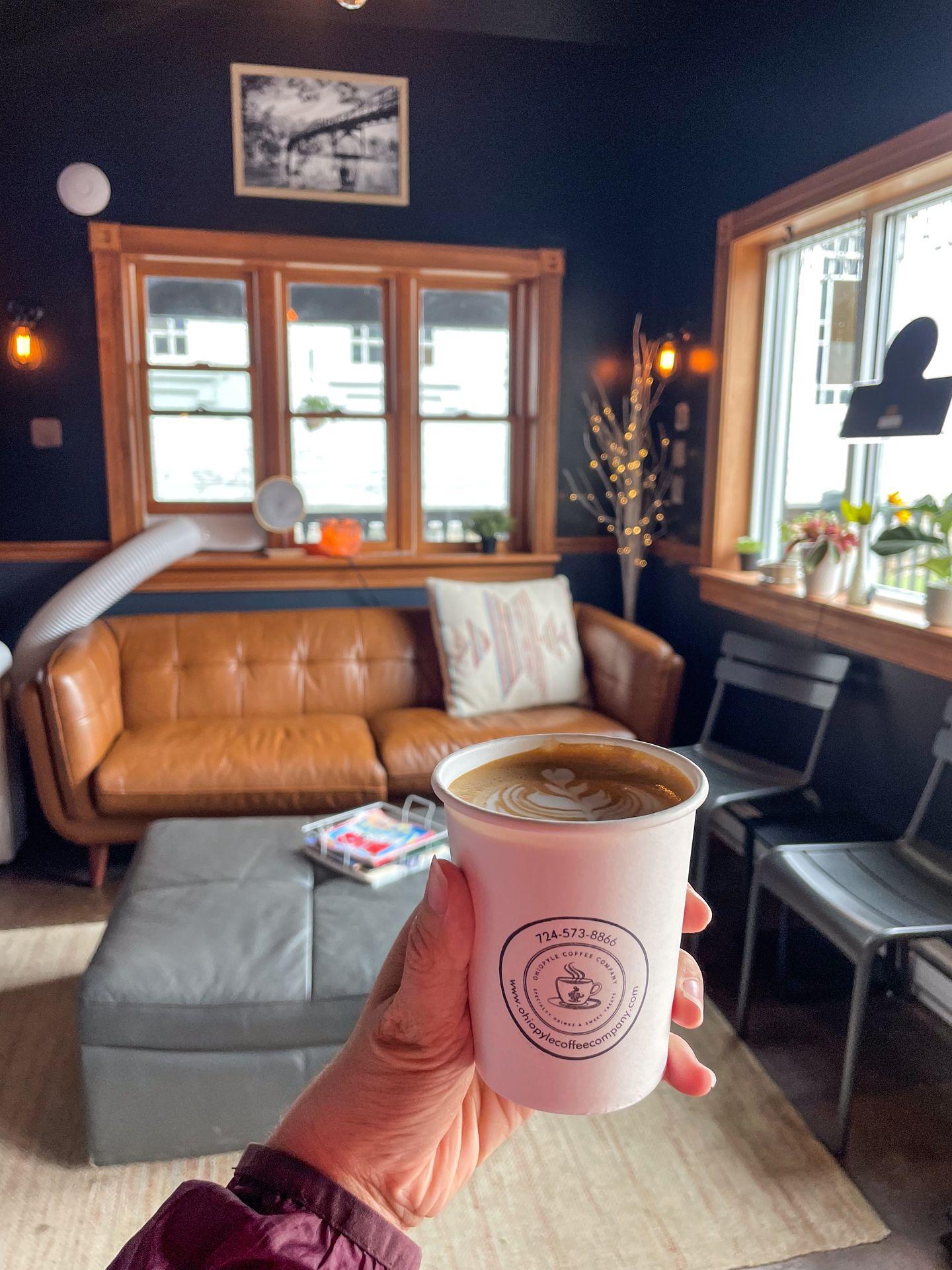 Holding up a coffee in a white, paper cup inside of Ohiopyle Coffee Company.