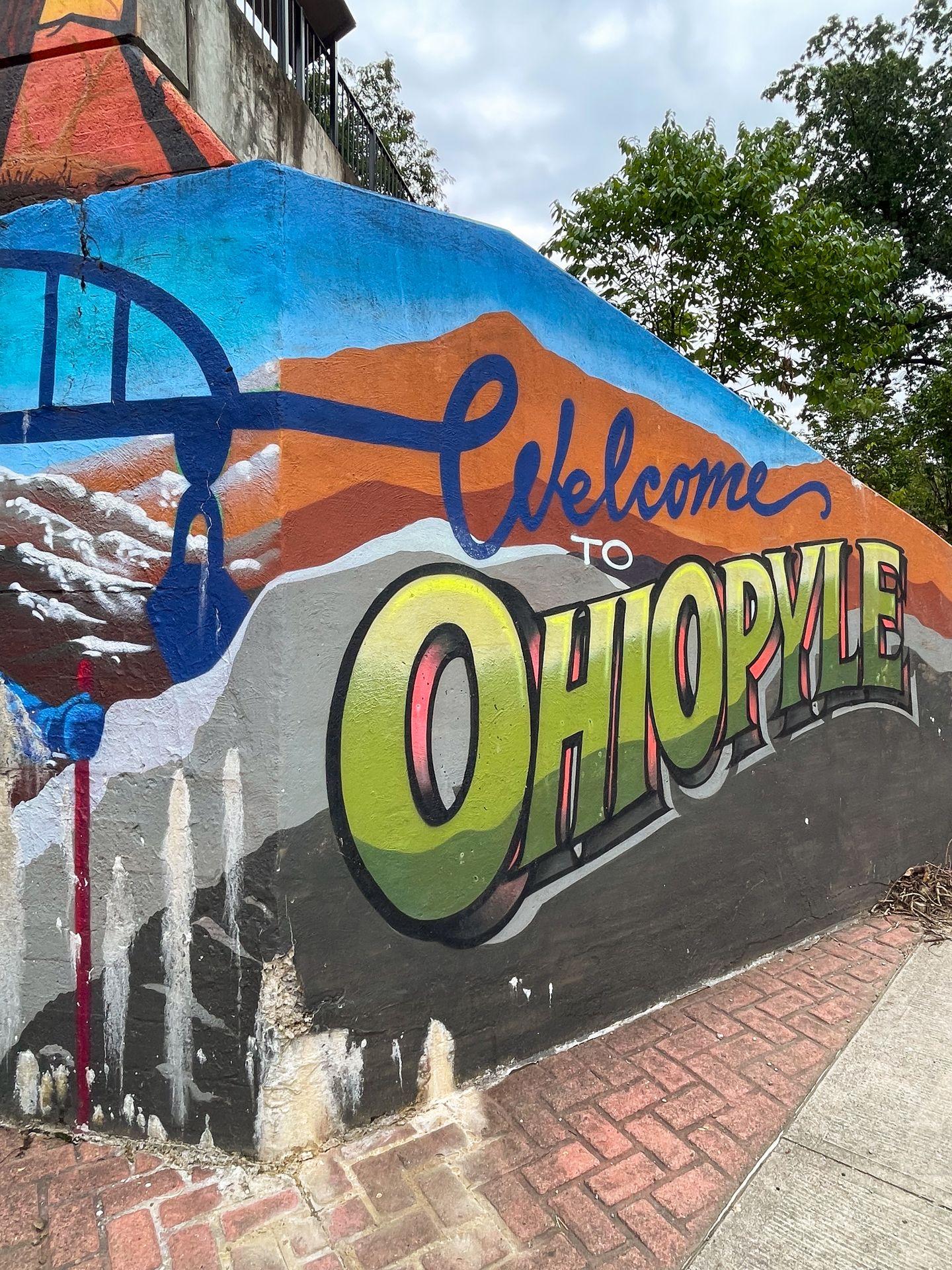 A mural over a corner that reads "Welcome to Ohiopyle" written in blue and green letters.