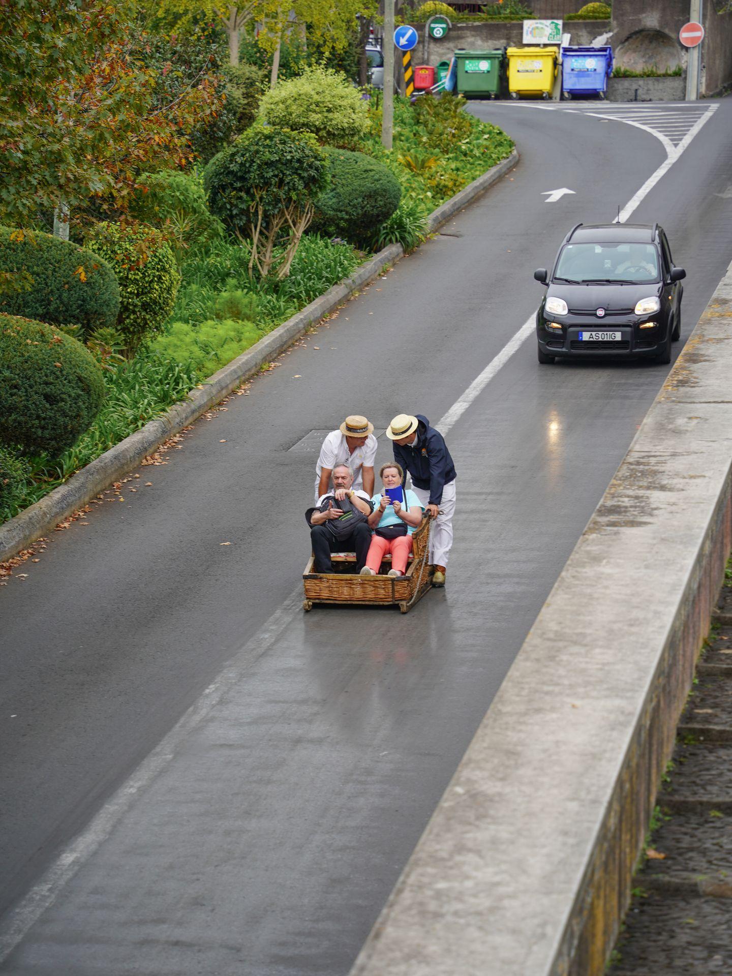 People being pushed in a wicker basket on a steep road.