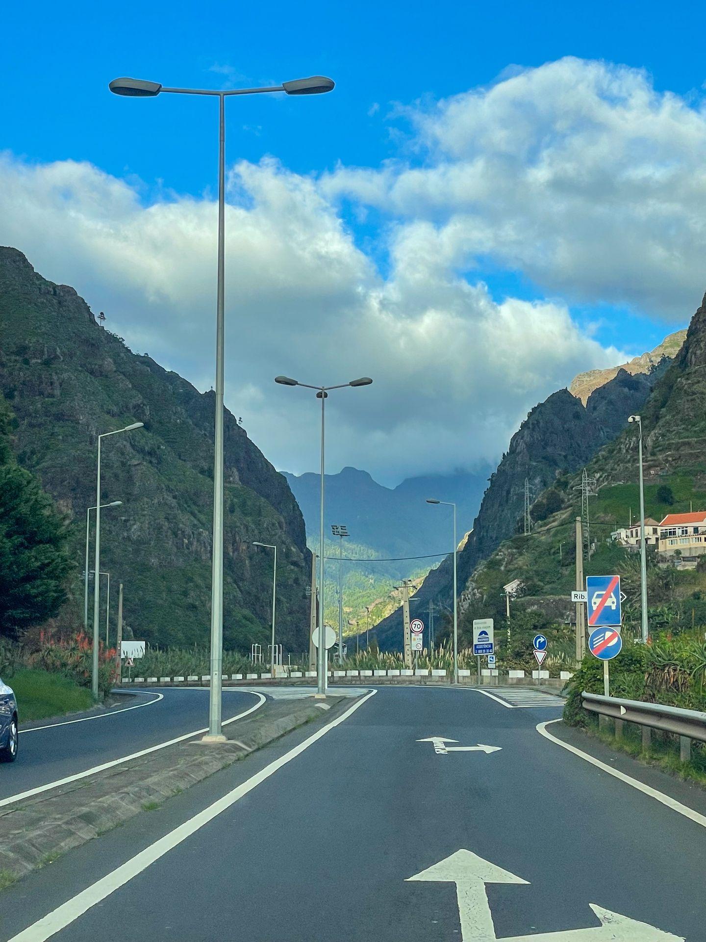A view of driving in Madeira. The road is surrounded by tall, green mountains.