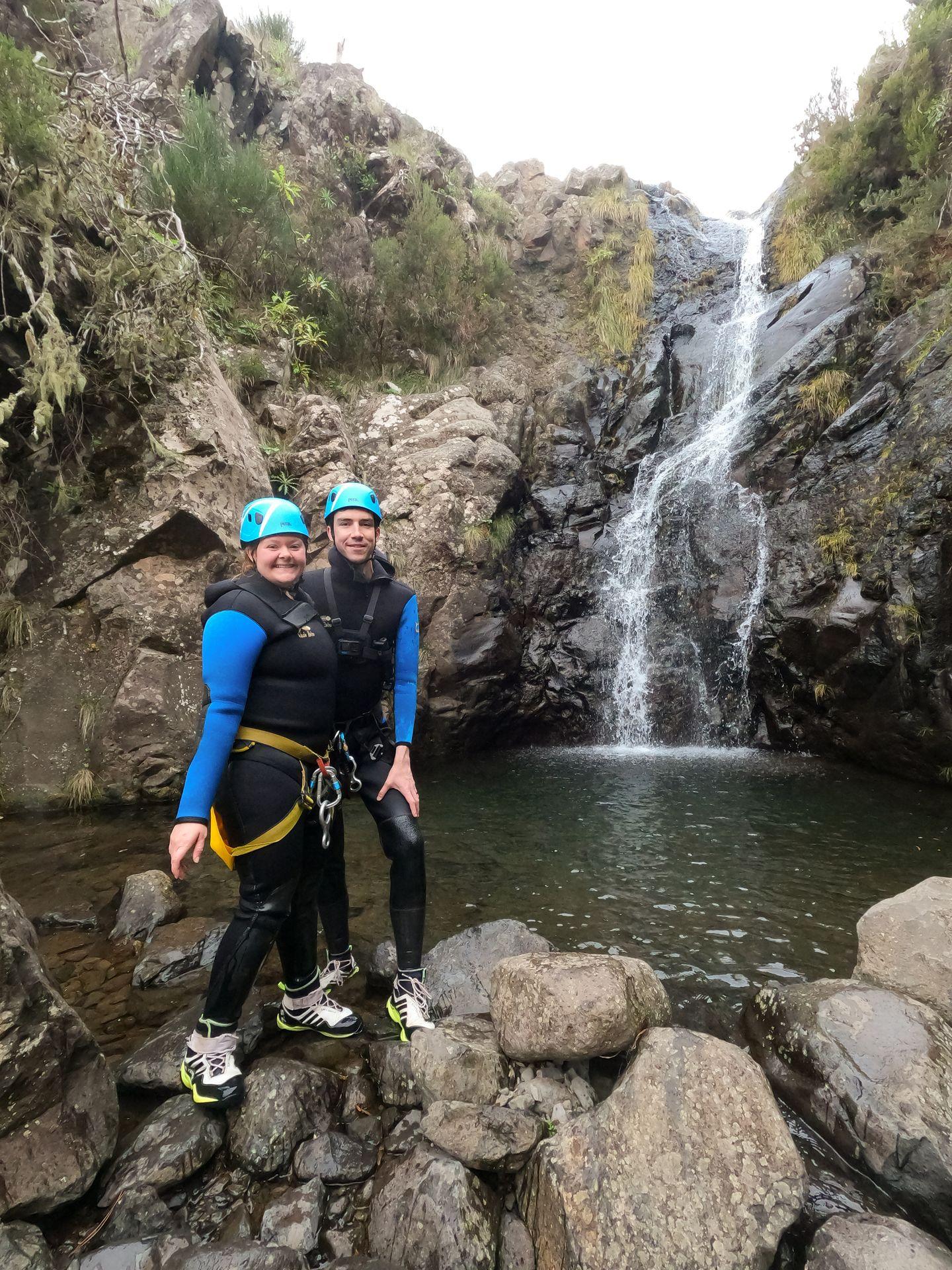 Lydia and Joe standing in front of a waterfall wearing wet suits while canyoneering in Madeira