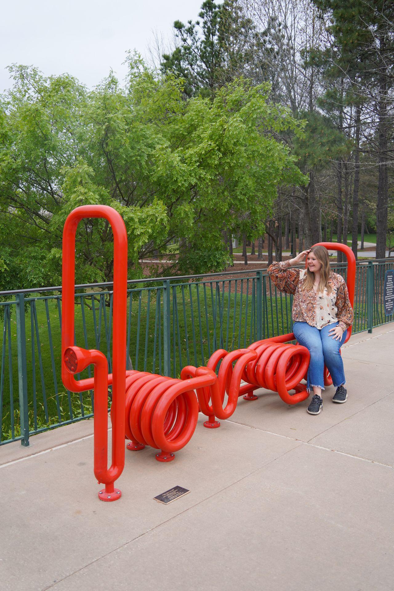 Lydia sitting on a red bench that spells 'love' using various tubes
