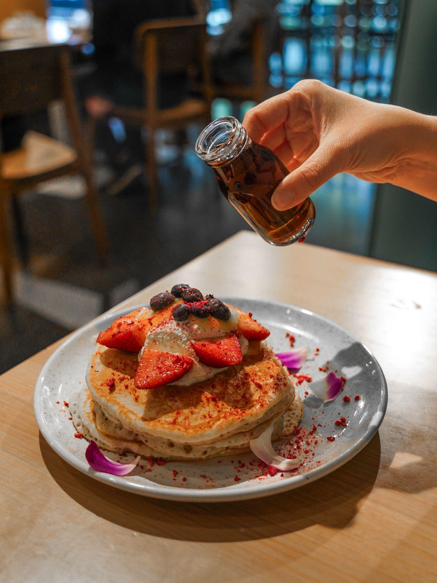 Holding up syrup over a plate of lemon ricotta pancakes