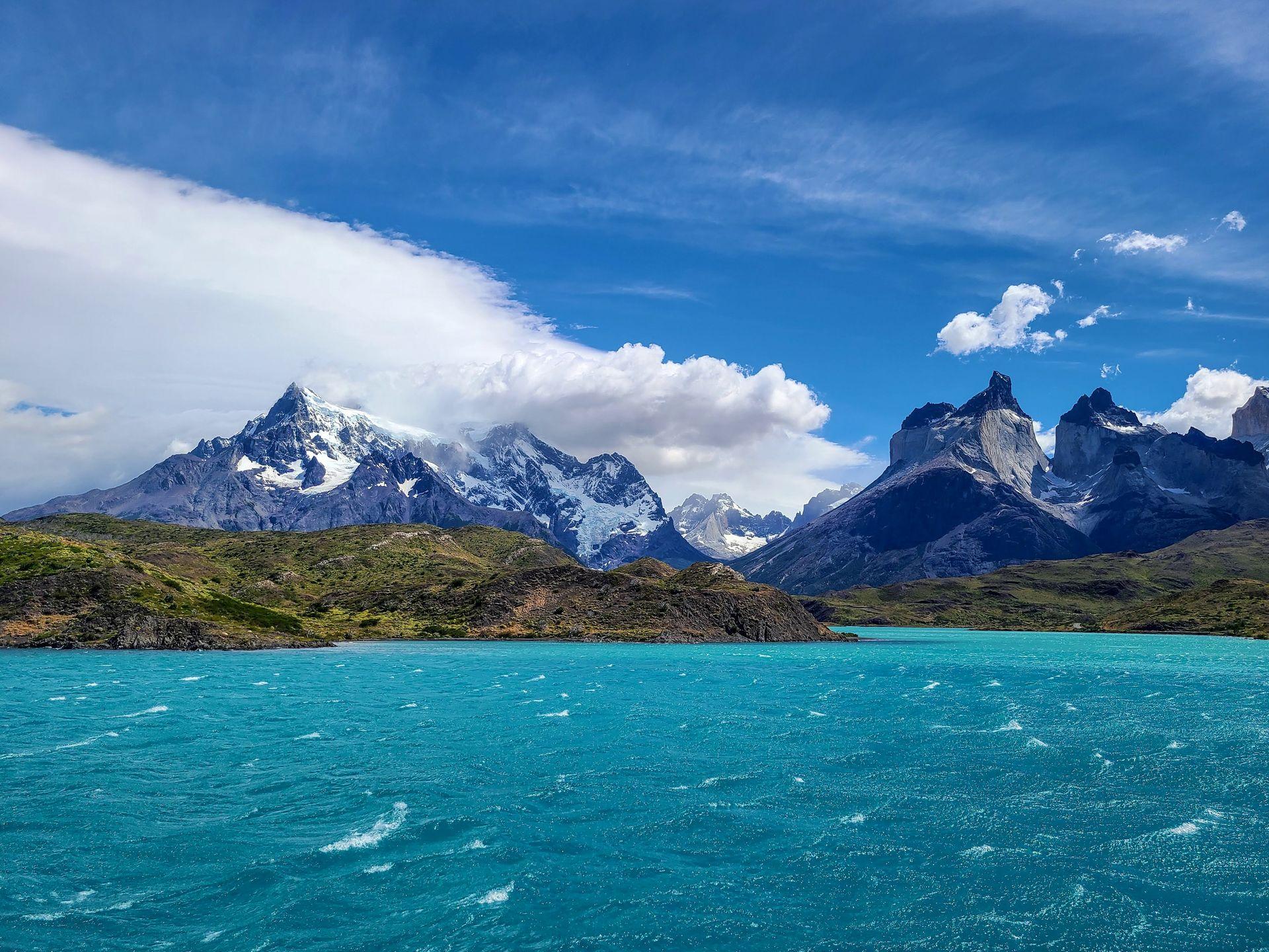 The view from riding the catamaran across Lake Pehoe. The water is a bright, aqua blue and there is a backdrop of mountains in the distance.