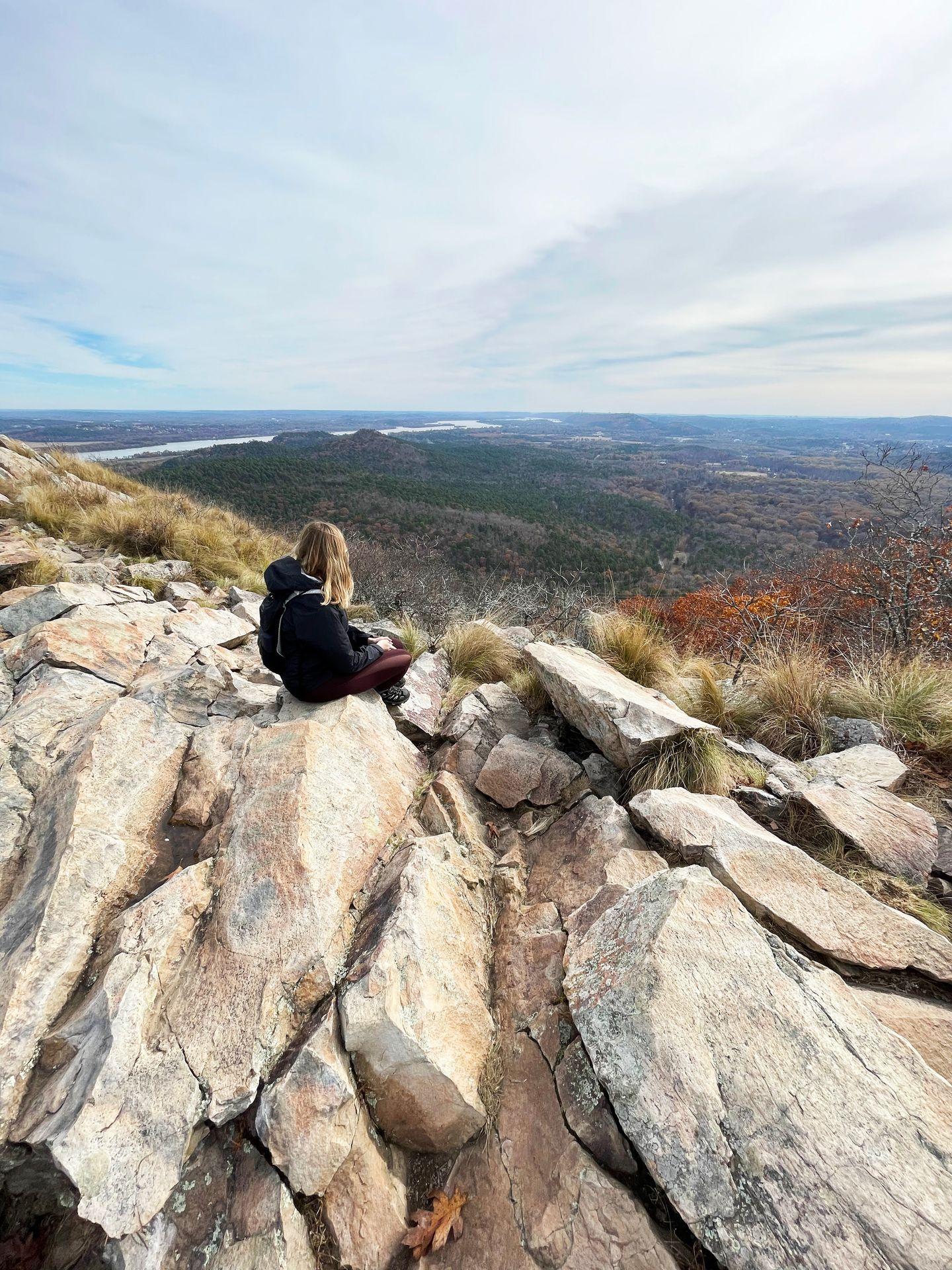 Lydia sitting on Pinnacle Mountain looking out at a view of the Arkansas River and the valley.