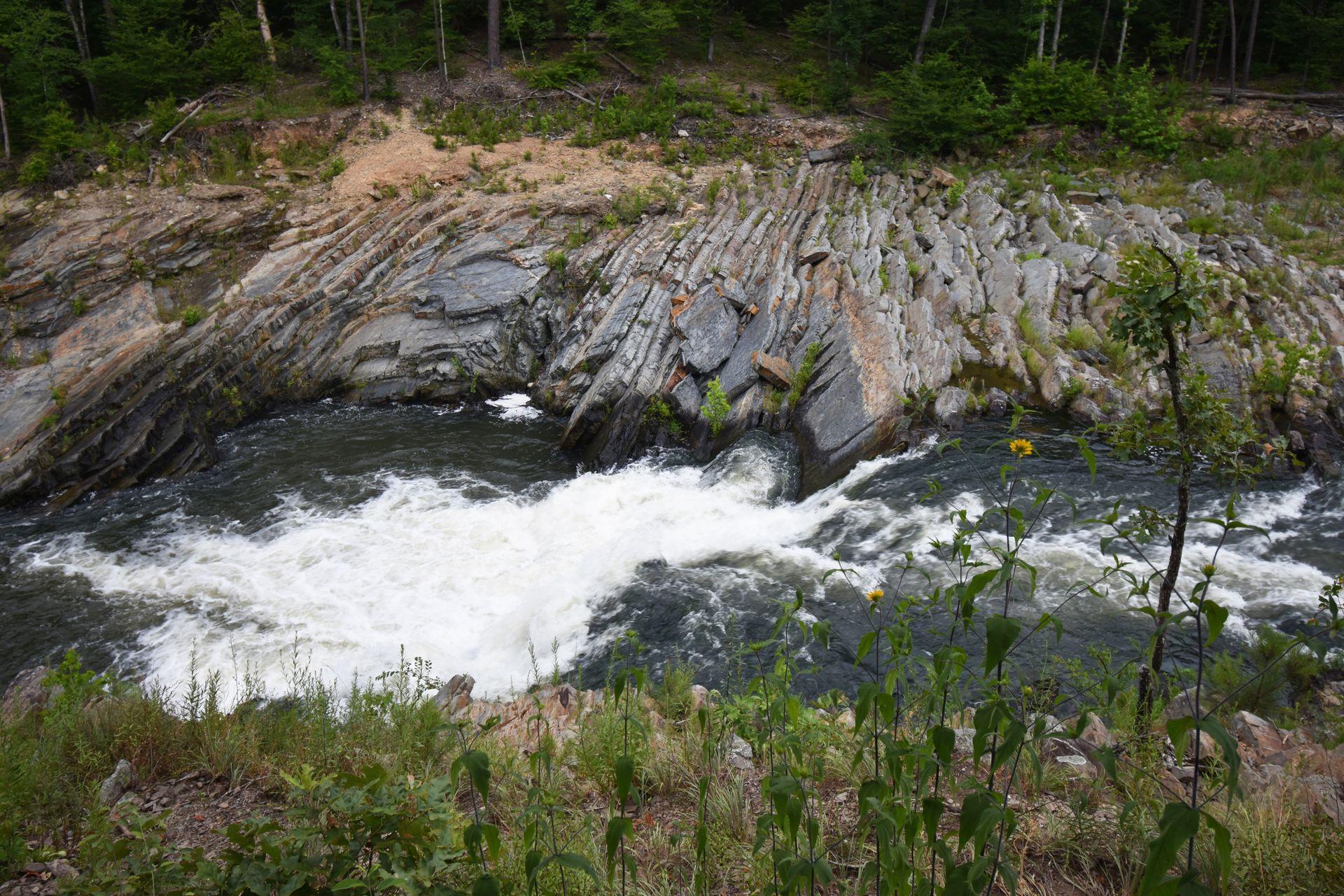 Looking down at the river along the Friends Loop trail. There are interesting rocks next to the water and greenery on both sides of the water.