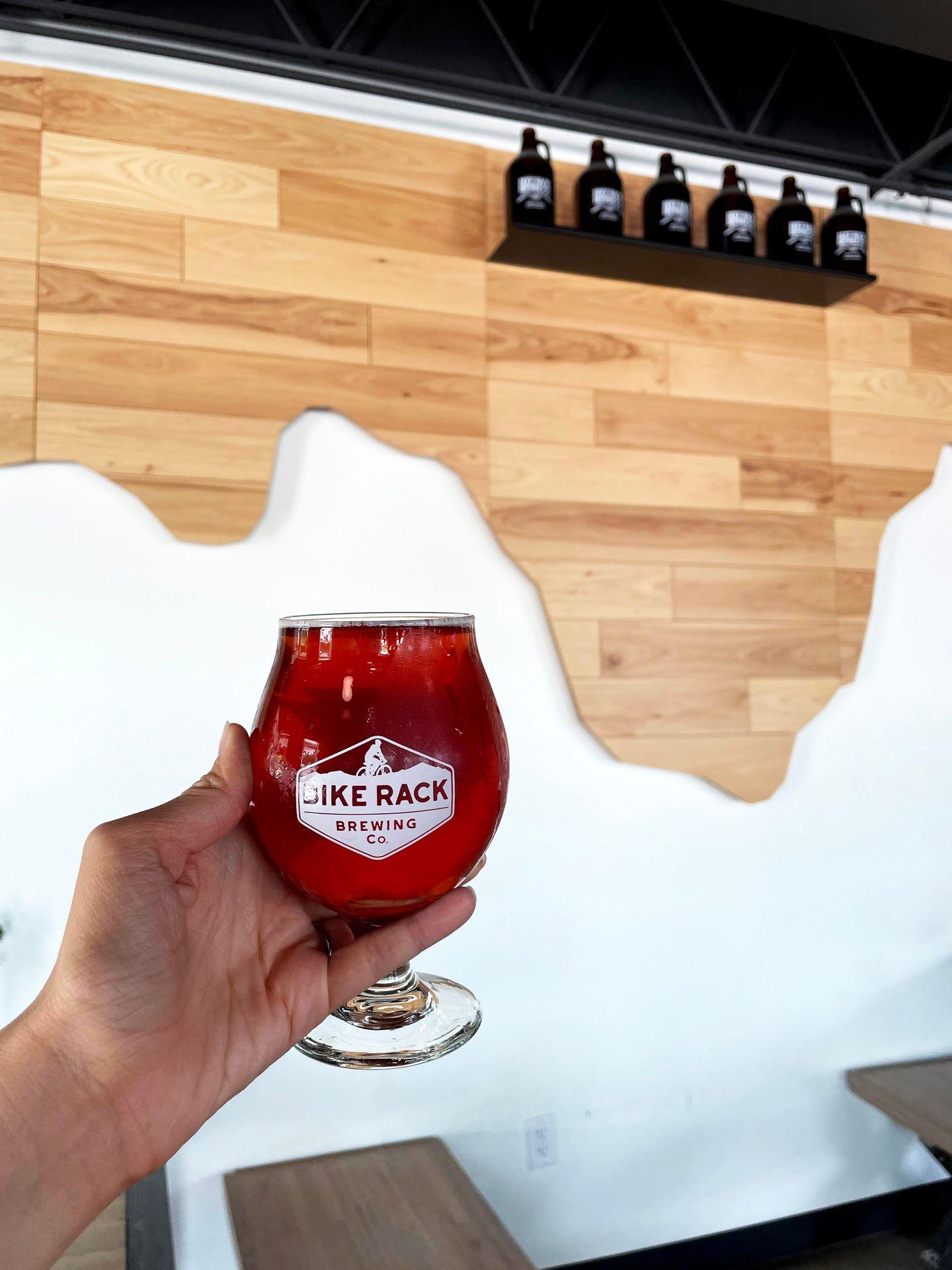 Holding up a red glass of beer with a wooden map on the wall behind it.