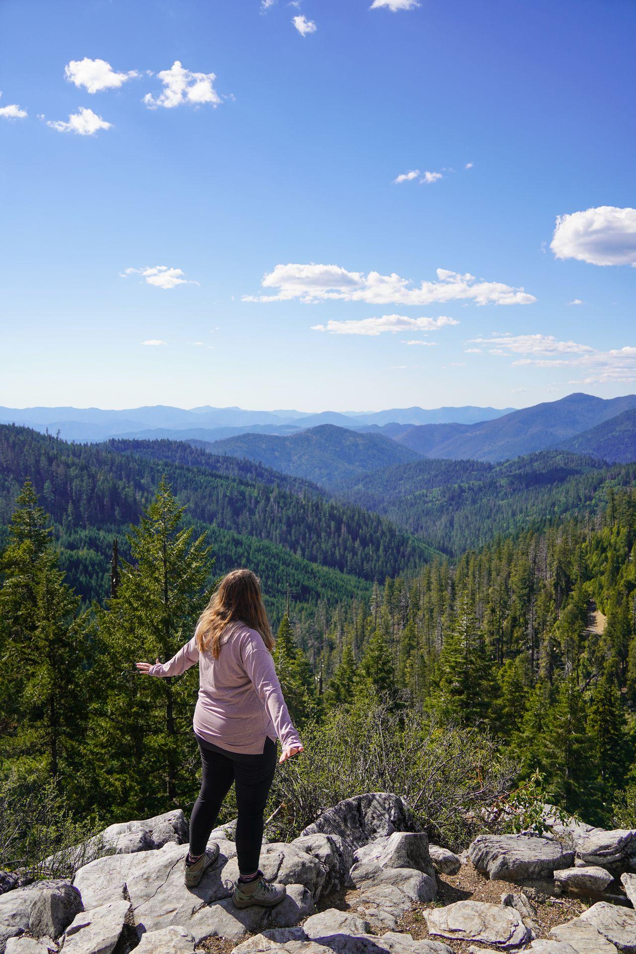 Lydia standing on rocks looking out a view of mountains in the distance