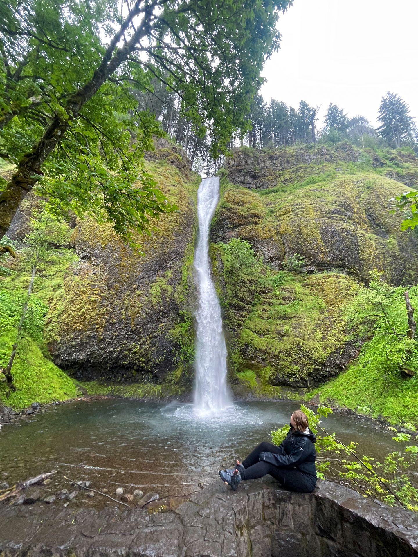 Lydia sitting on a stone wall looking at Horsetail Falls