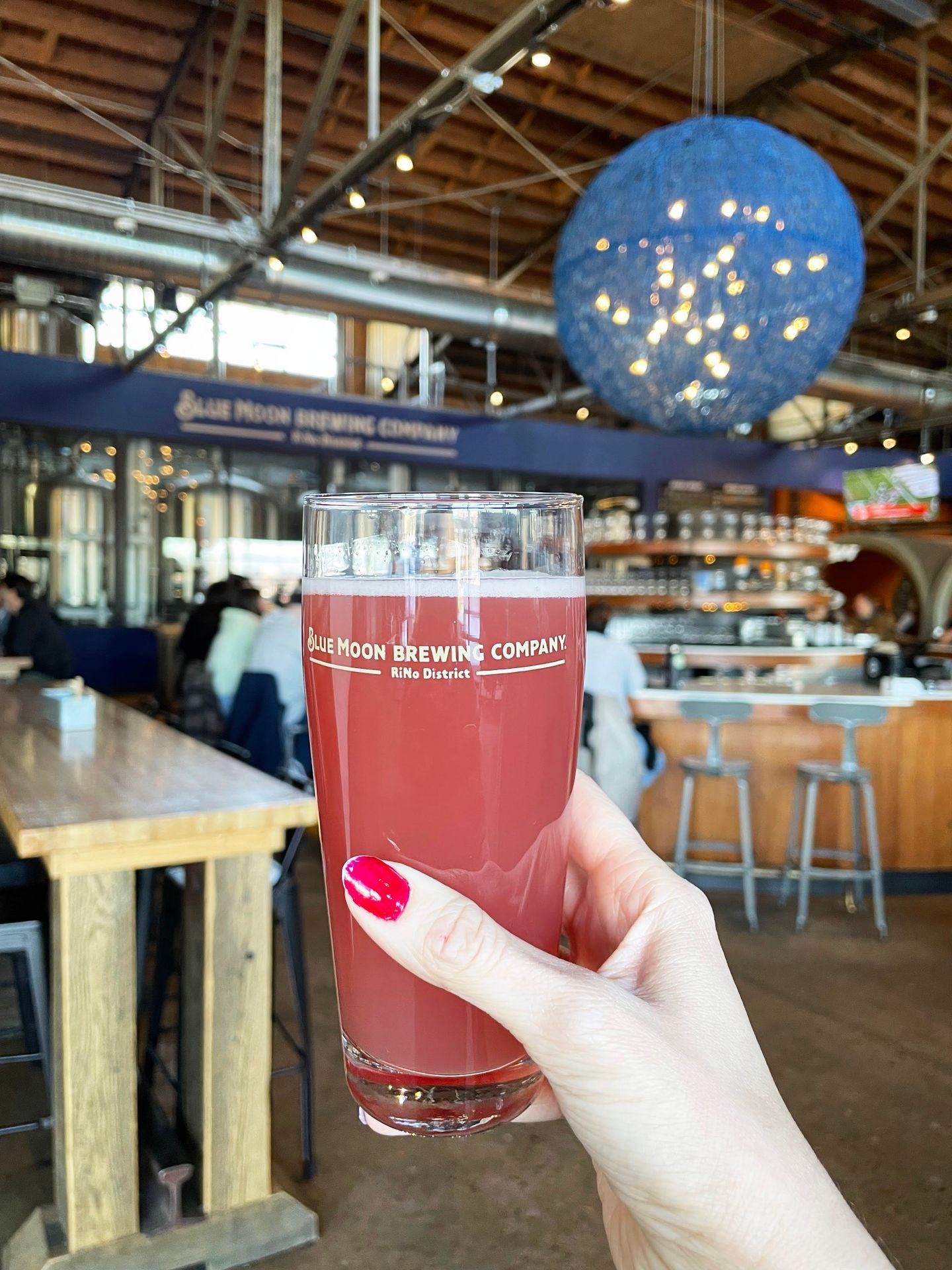 Holding up a pint of beer at the Blue Moon Brewery. In the background, there is a giant blue ball hanging from the ceiling.