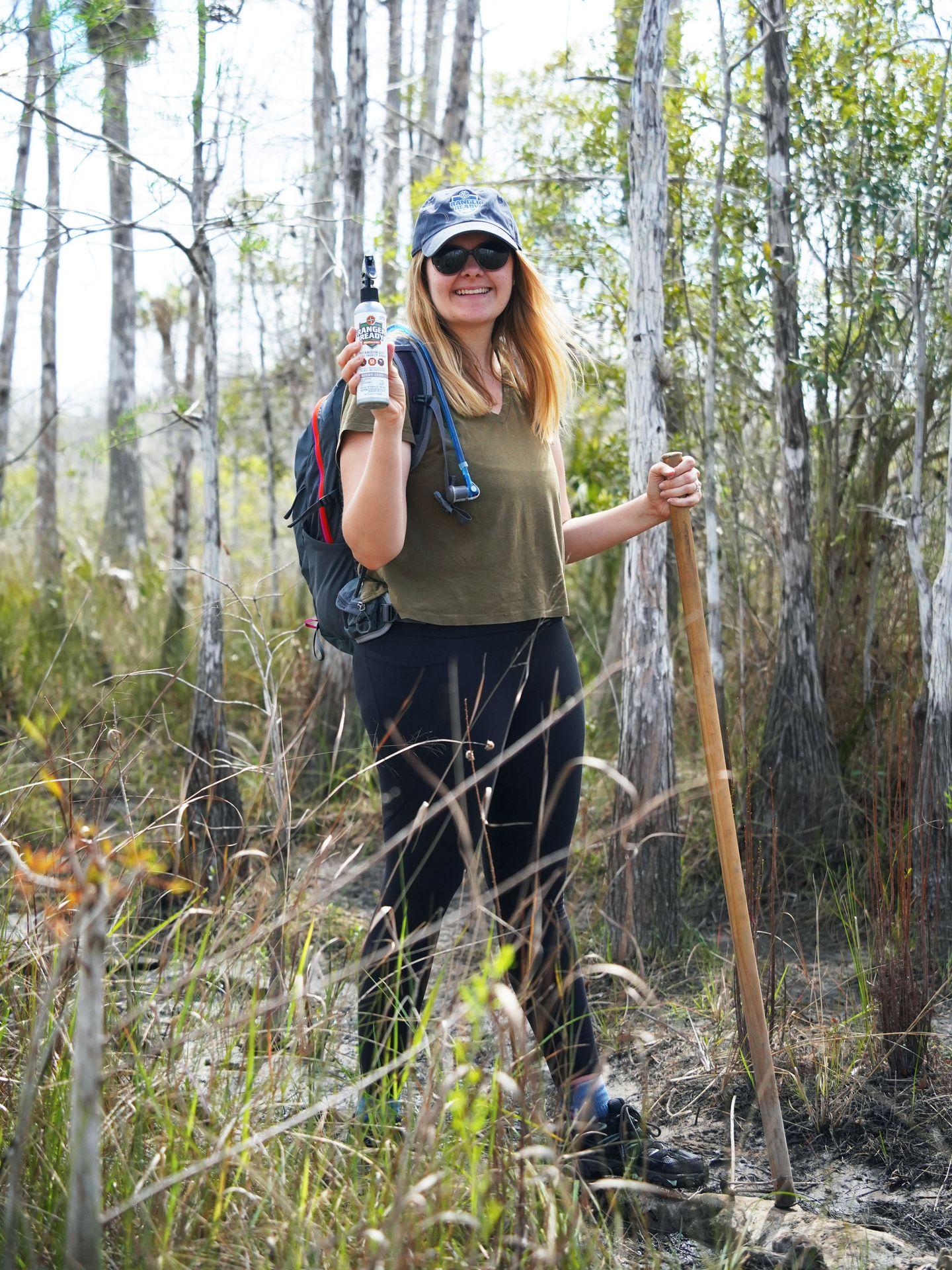 Lydia standing with a hiking pole on a trail in Big Cypress Preserve. She holds a can of Ranger Ready bug spray.