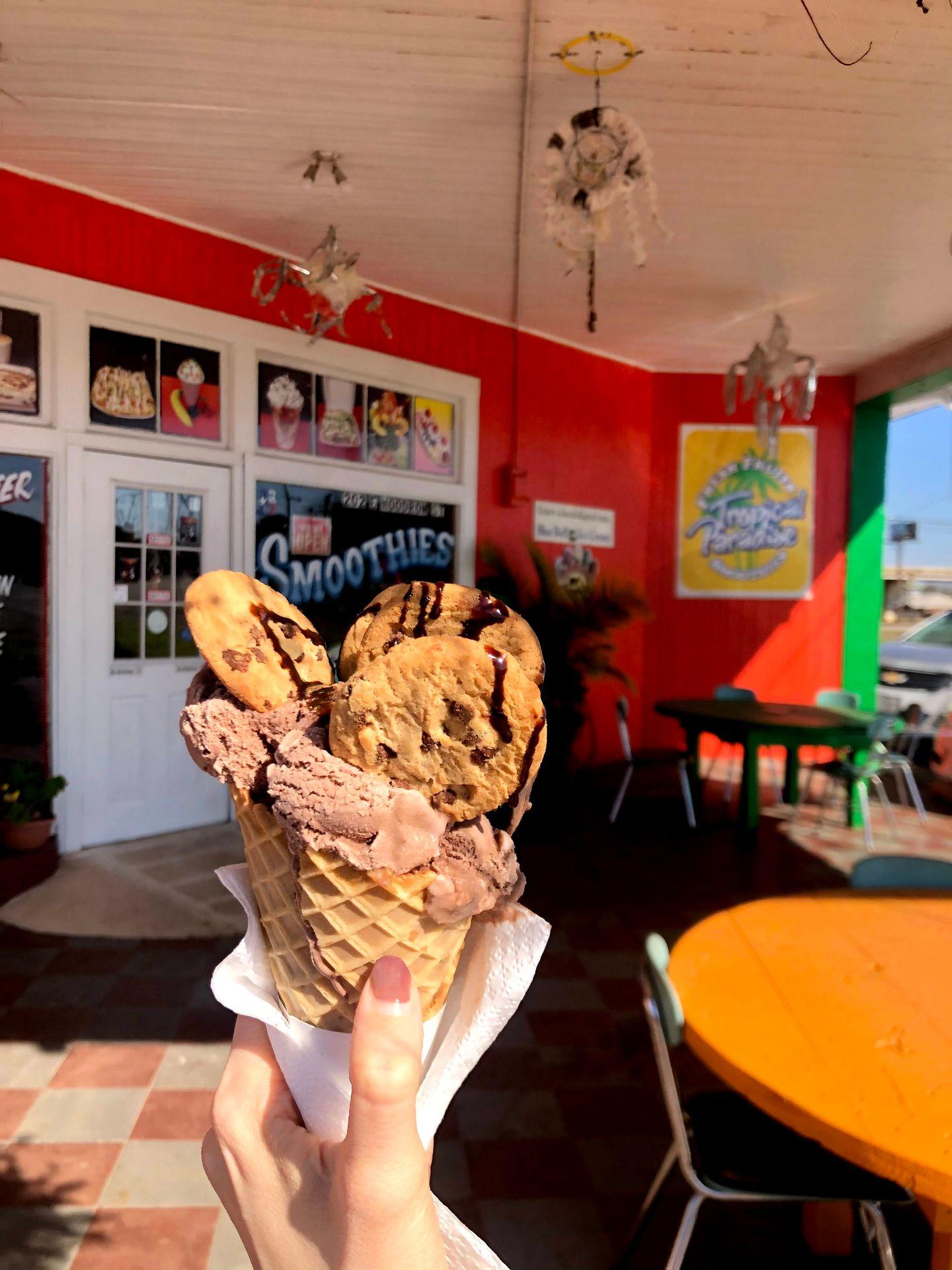 Holding up an ice cream cone with chocolate ice cream, cookies sticking out of it and chocolate syrup drizzled on top
