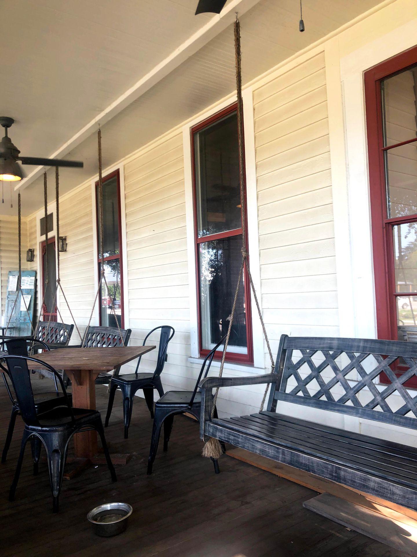 A porch a swinging bench next to a table and chairs