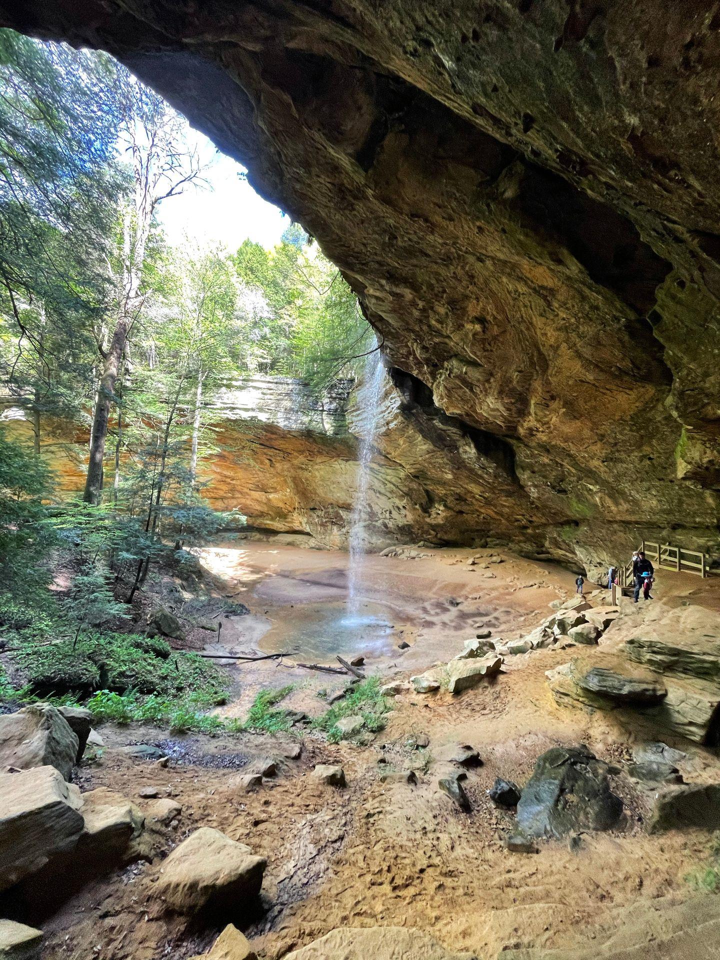 A view of Ash Cave and a waterfall coming from the top from the side of a rock cliff.