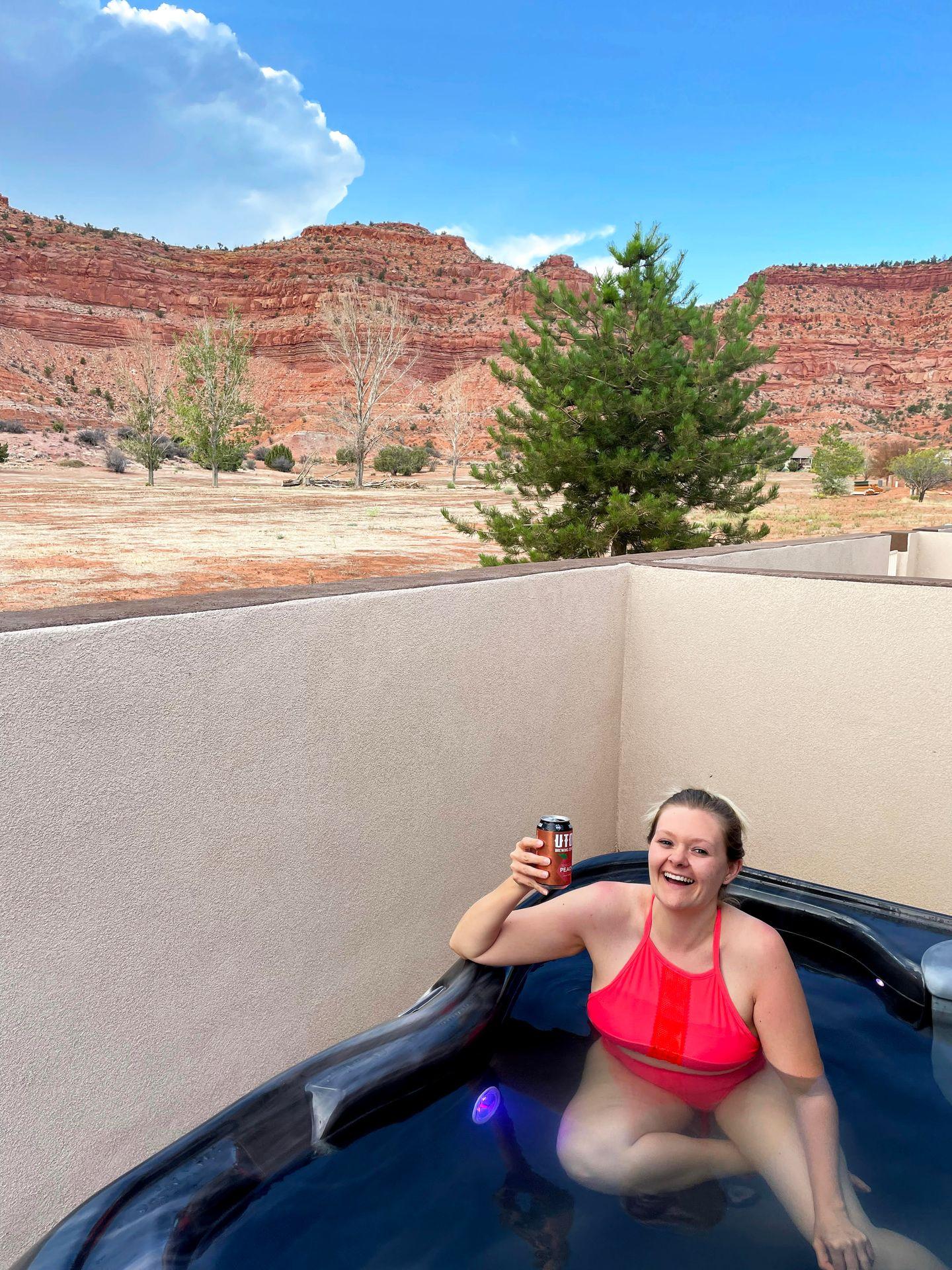 Lydia in a hot tub with views of orange mountains in the background.