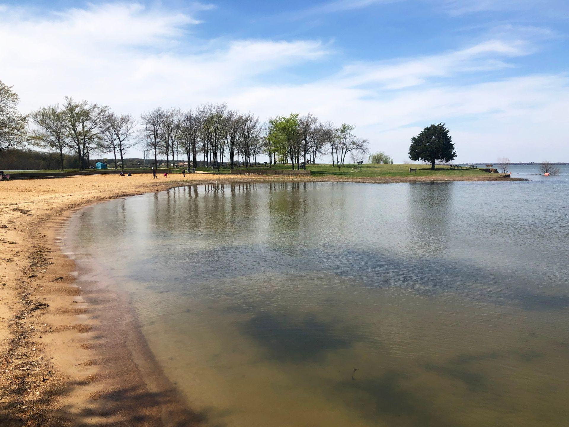 A lake with a small beach area and some trees in the distance.
