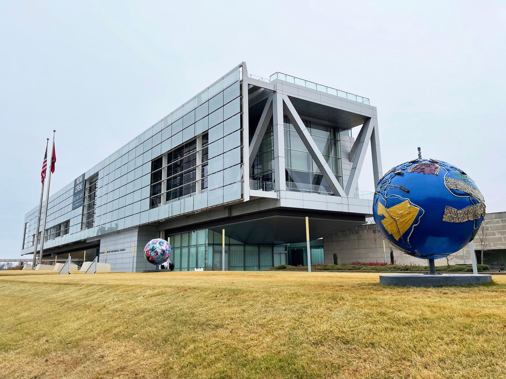 A view of the outside of the Clinton Museum and Library. The building is long and rectangular and an earth sculpture sits in front.