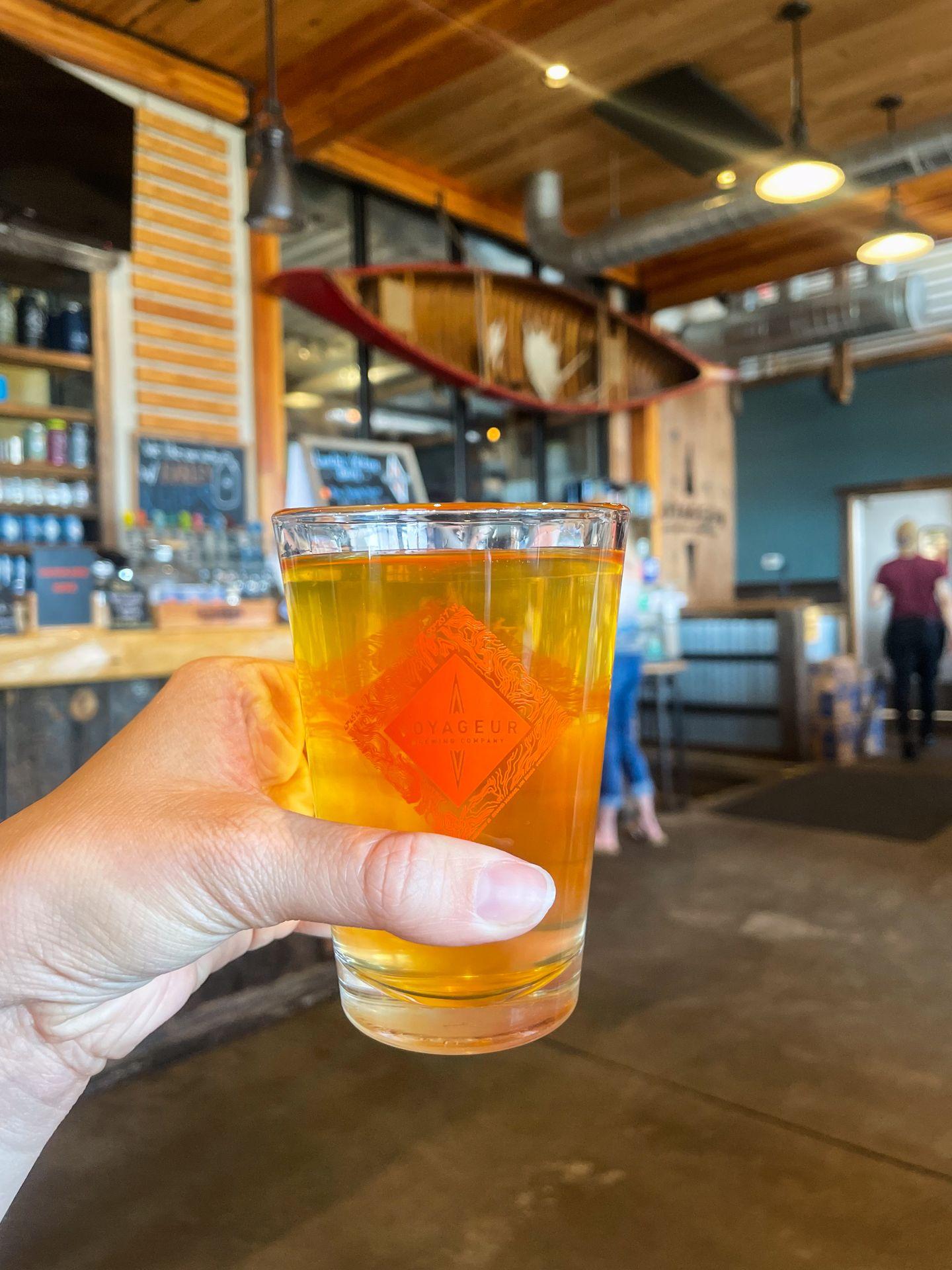 Holding up a beer inside of Voyageur Brewing Company
