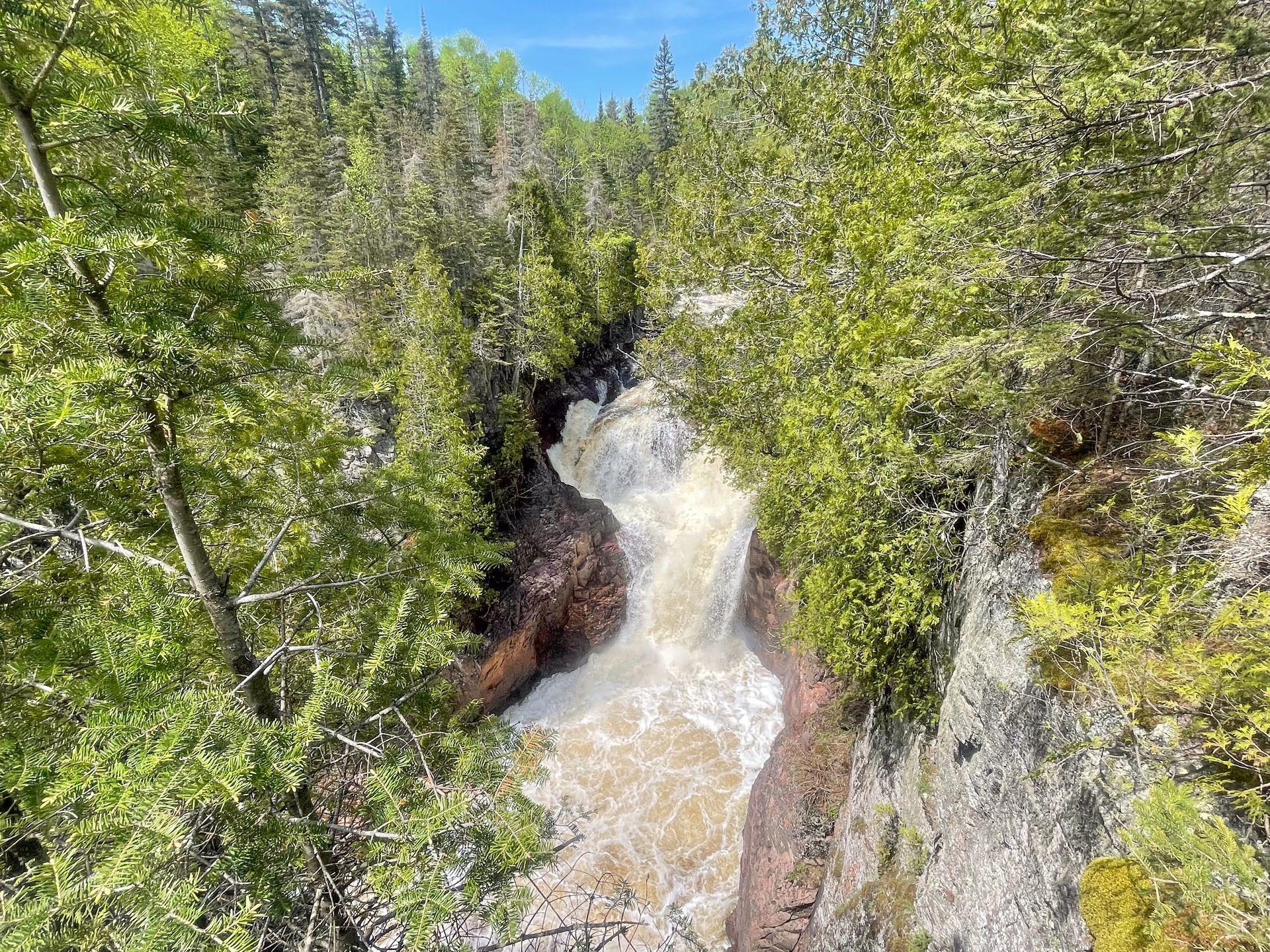 A strong waterfall glowing through a narrow gorge. It is partially obscured by trees.