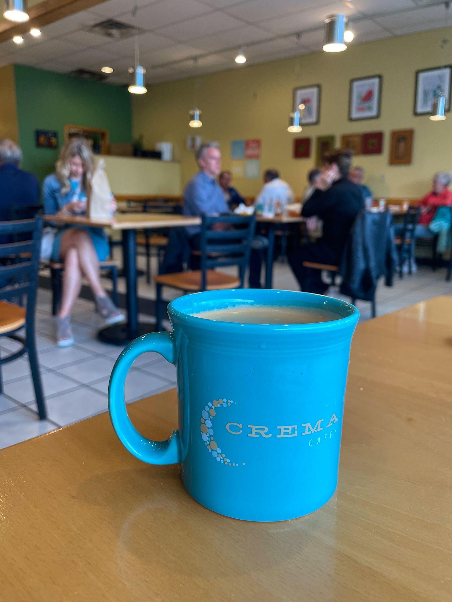 A blue mug with coffee sitting on a table inside of Crema Cafe in Madison