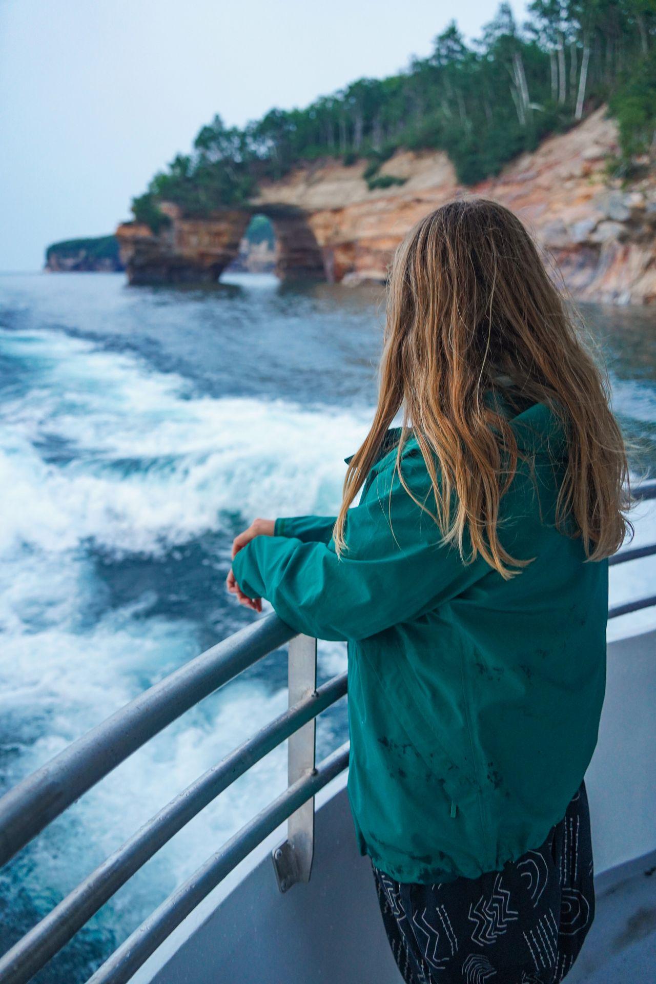 Lydia standing on the balcony of the boat and looking over at a giant arch