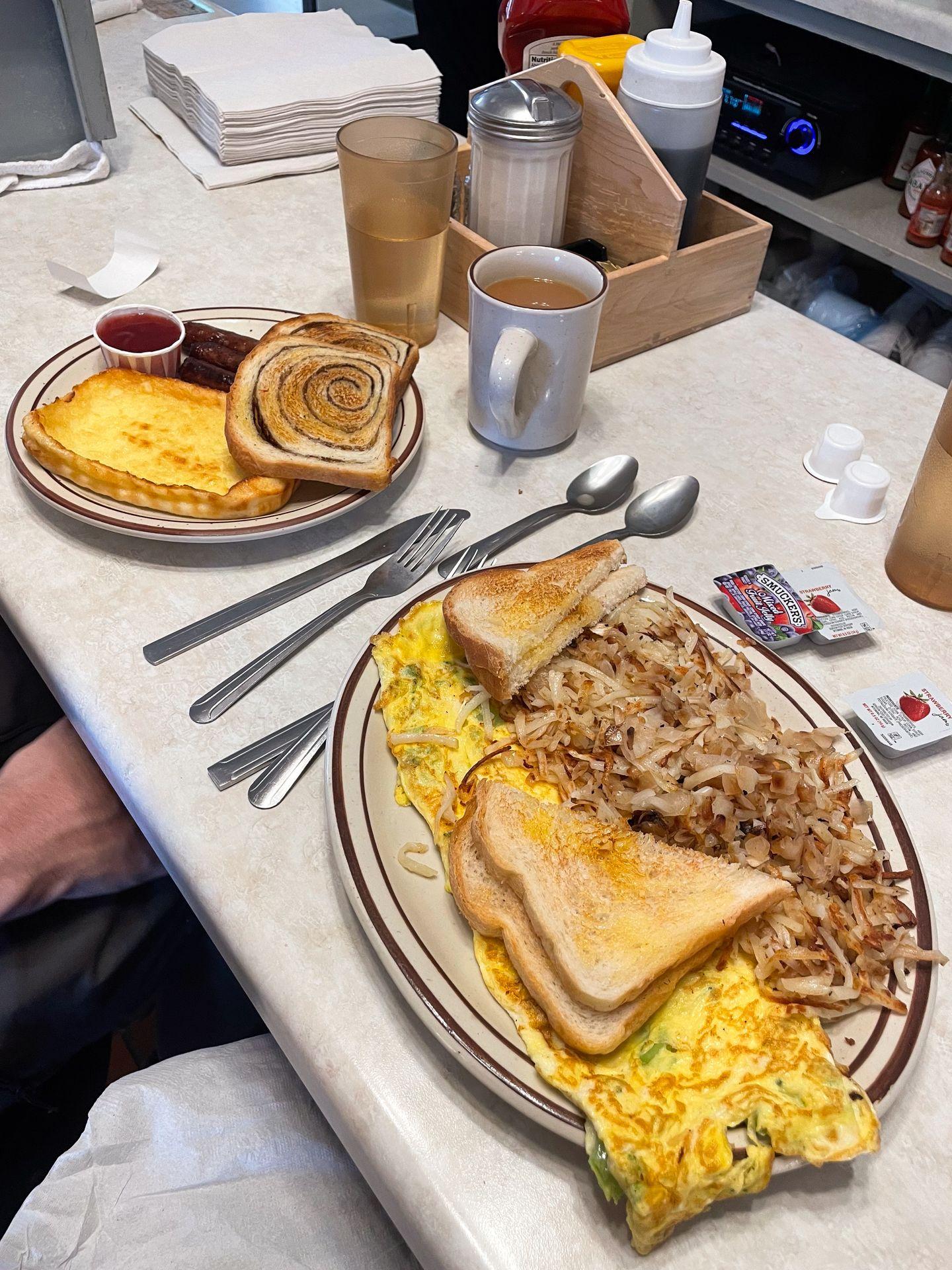 Two plates of breakfast food from Suomi Home Bakery & Restaurant. There is scrambled eggs, toast, hashbrowns and Finnish pastries.