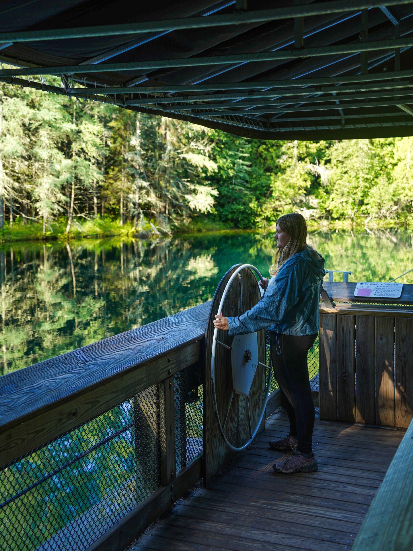 Lydia standing at a large steering wheel on the raft at Kitch-iti-kipi
