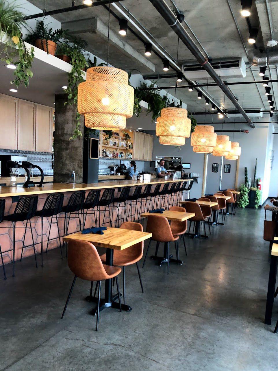 A pink bar with small tables next to it. There is a row of neutral, hanging lights above the bar.