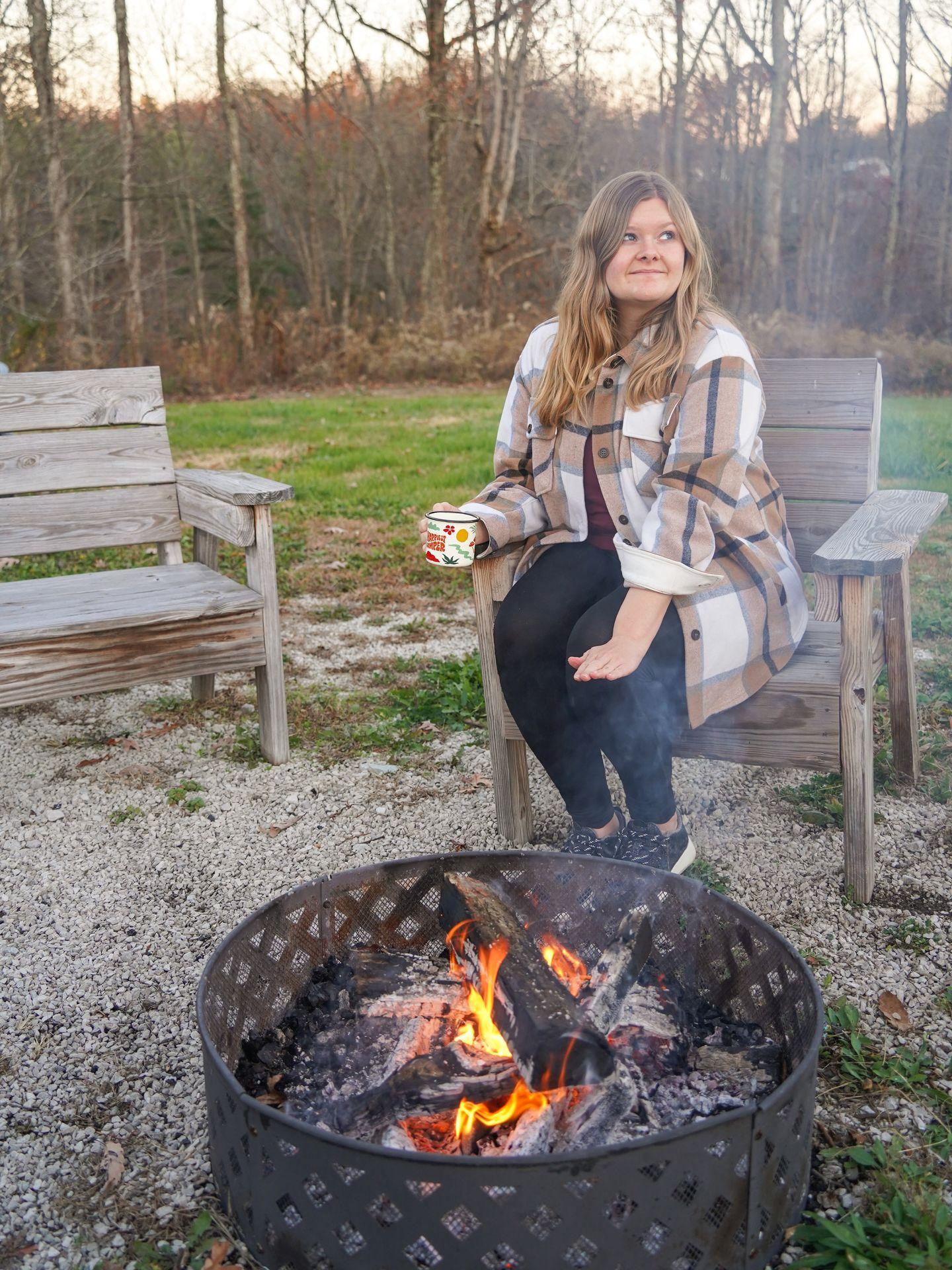 Lydia sitting next to the firepit at Boone's Bluff and warming her hands.