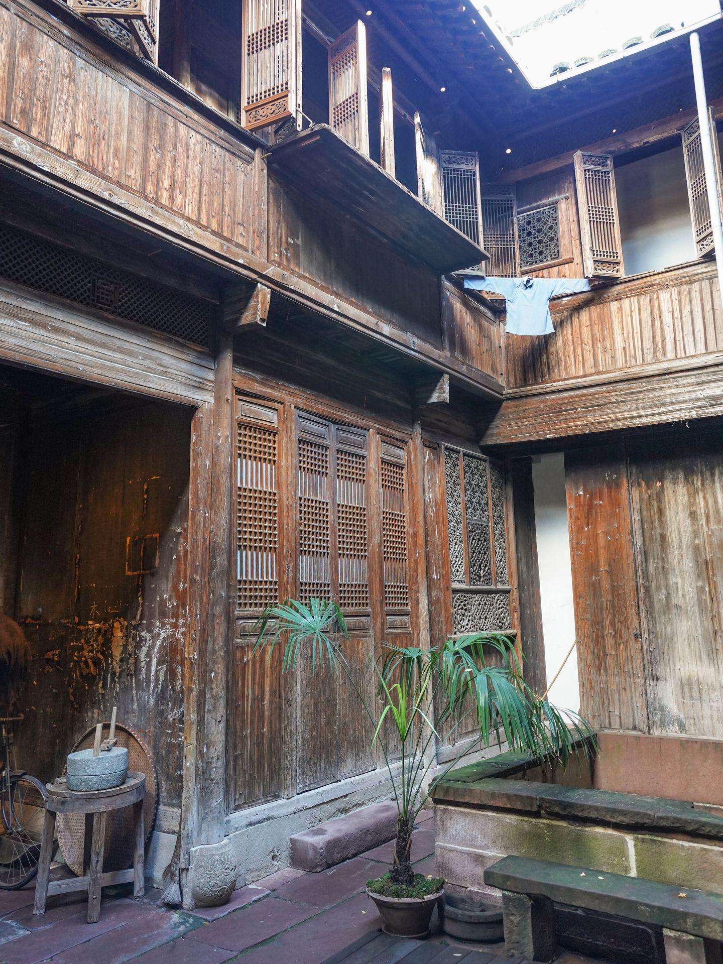 Inside of the Chinese Home inside of the Peabody Essex Museum. There are wooden panels, a hanging shirt and plants